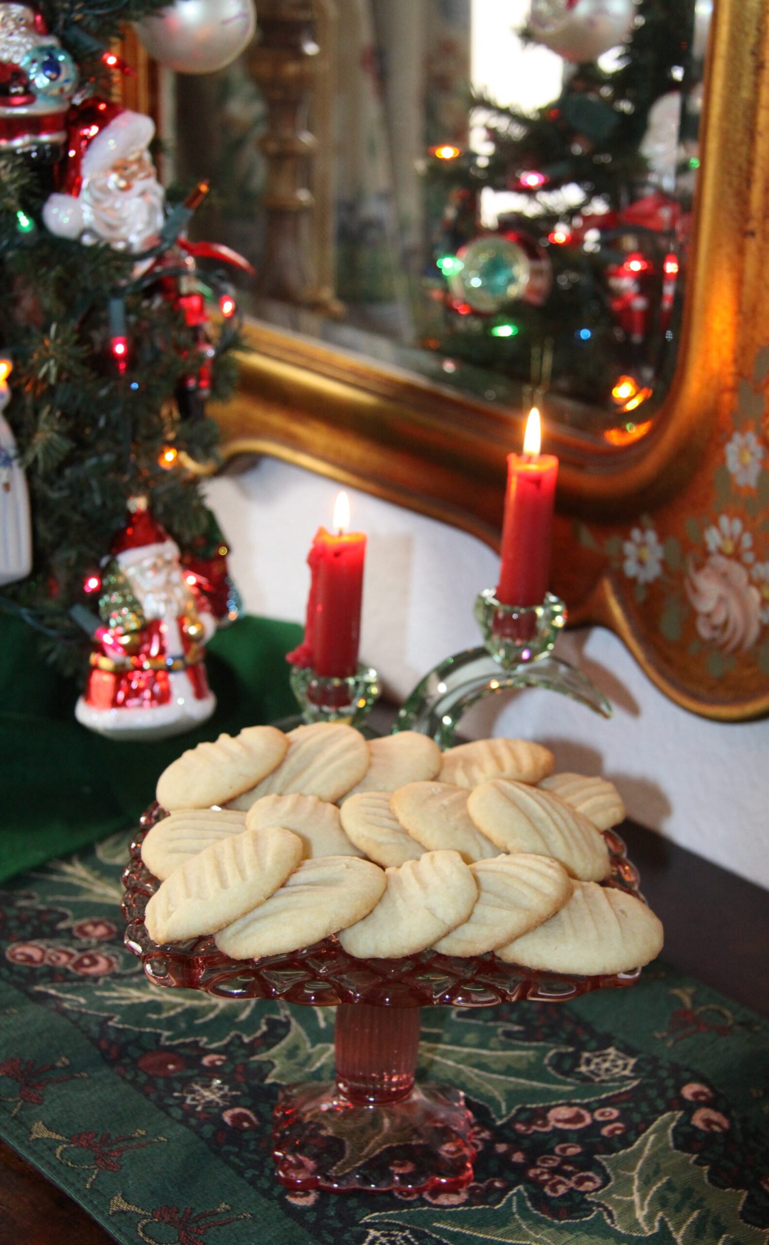 Butter cookies on a cake stand with Christmas decorations around it.