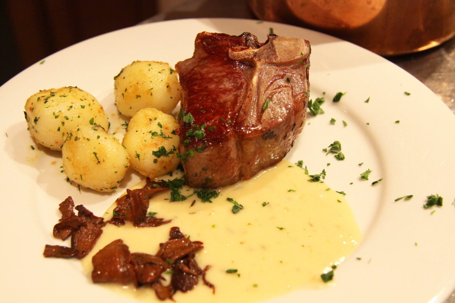 Pan fired lamb chops with garlic cream and porcini mushrooms served on a plate alongside small potatoes