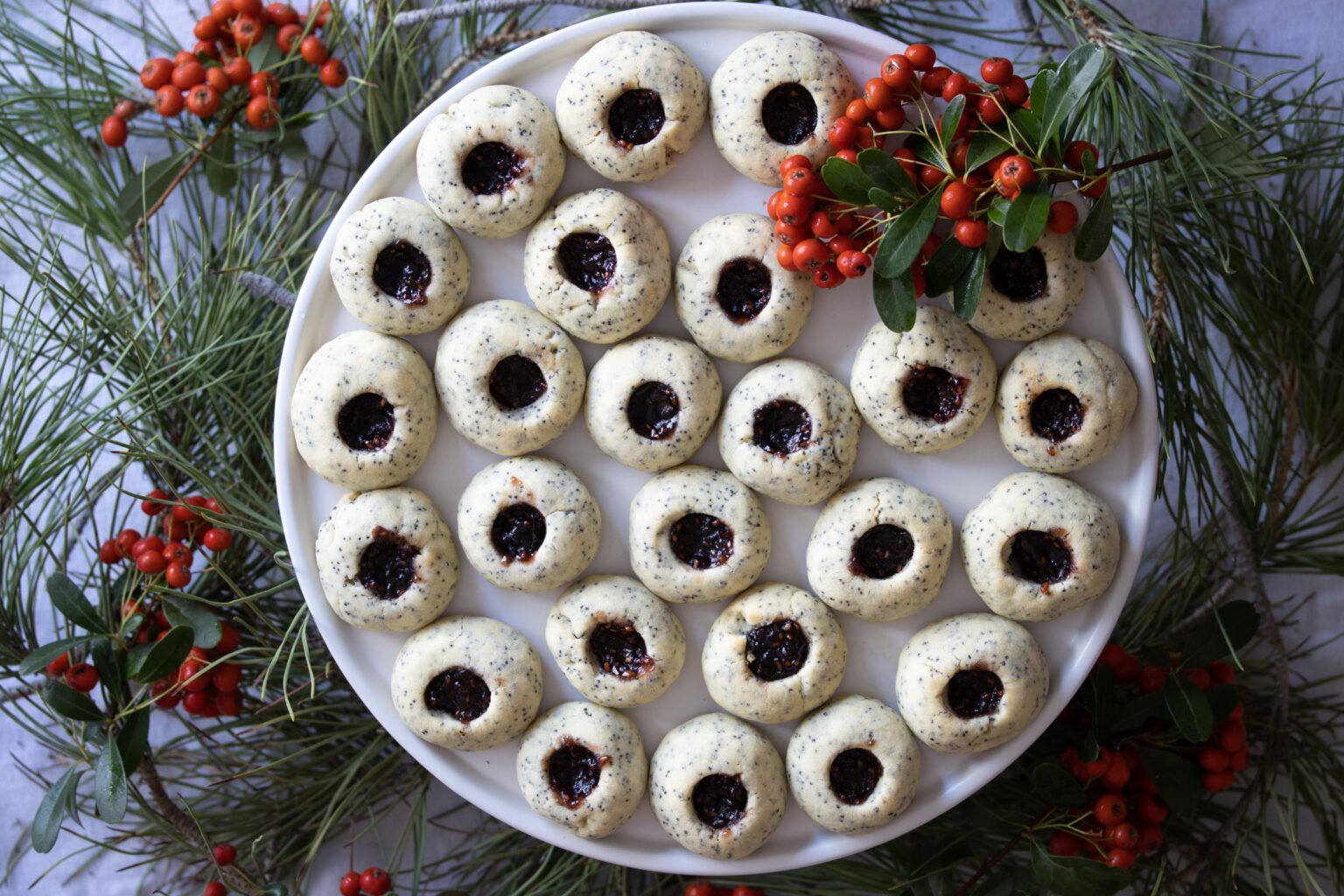 poppy seed thumbrint cookies in a plate surrounded by holiday holly