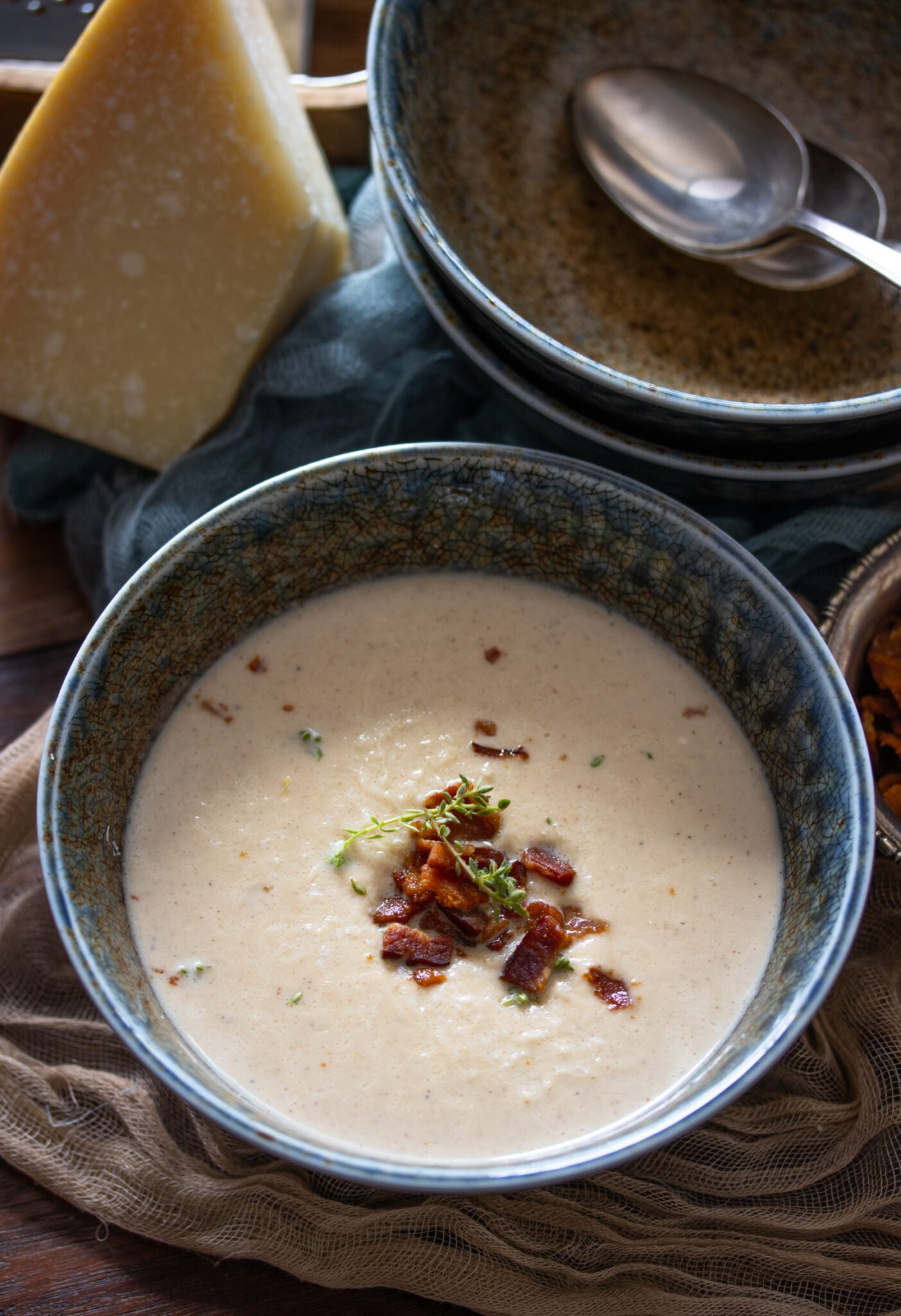 roasted cauliflower soup Roasted Cauliflower Soup in a blue bowl with bacon bits and parmesan cheese next to it