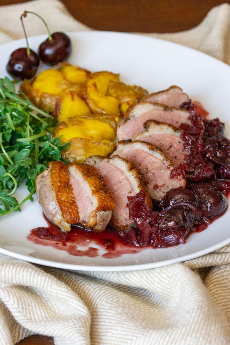 Duck Breast with Port and Cherry Sauce Duck breast with cherry sauce sliced and on a white plate