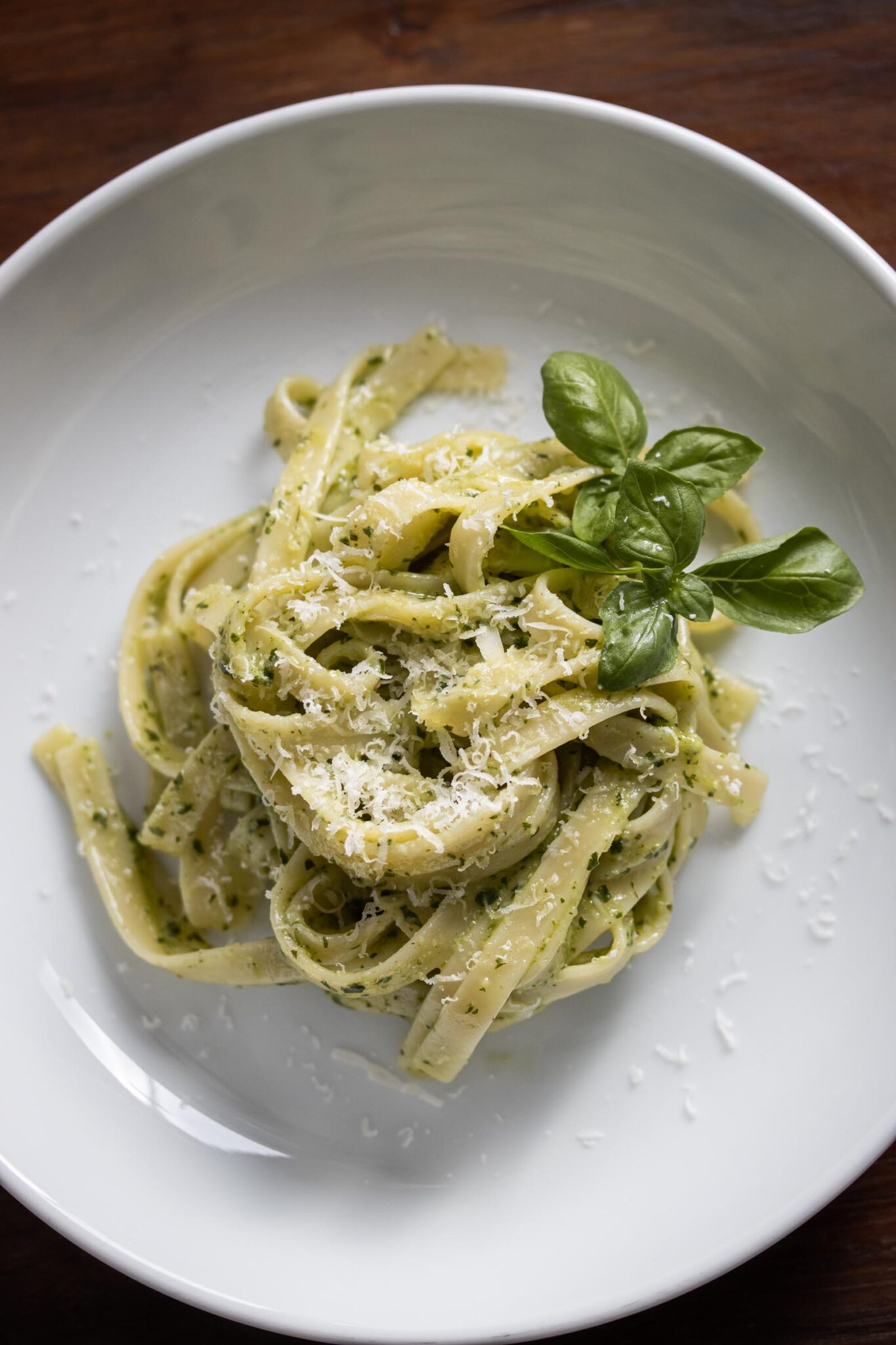 Close up of pesto pasta served in a white dish with lots of cheese sprinkled over it.
