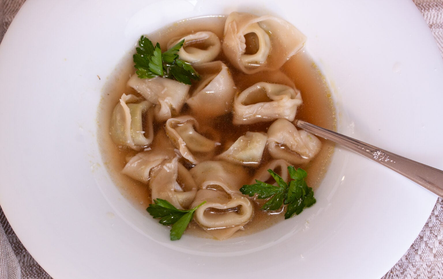 A white soup plate with tortellini with broth.