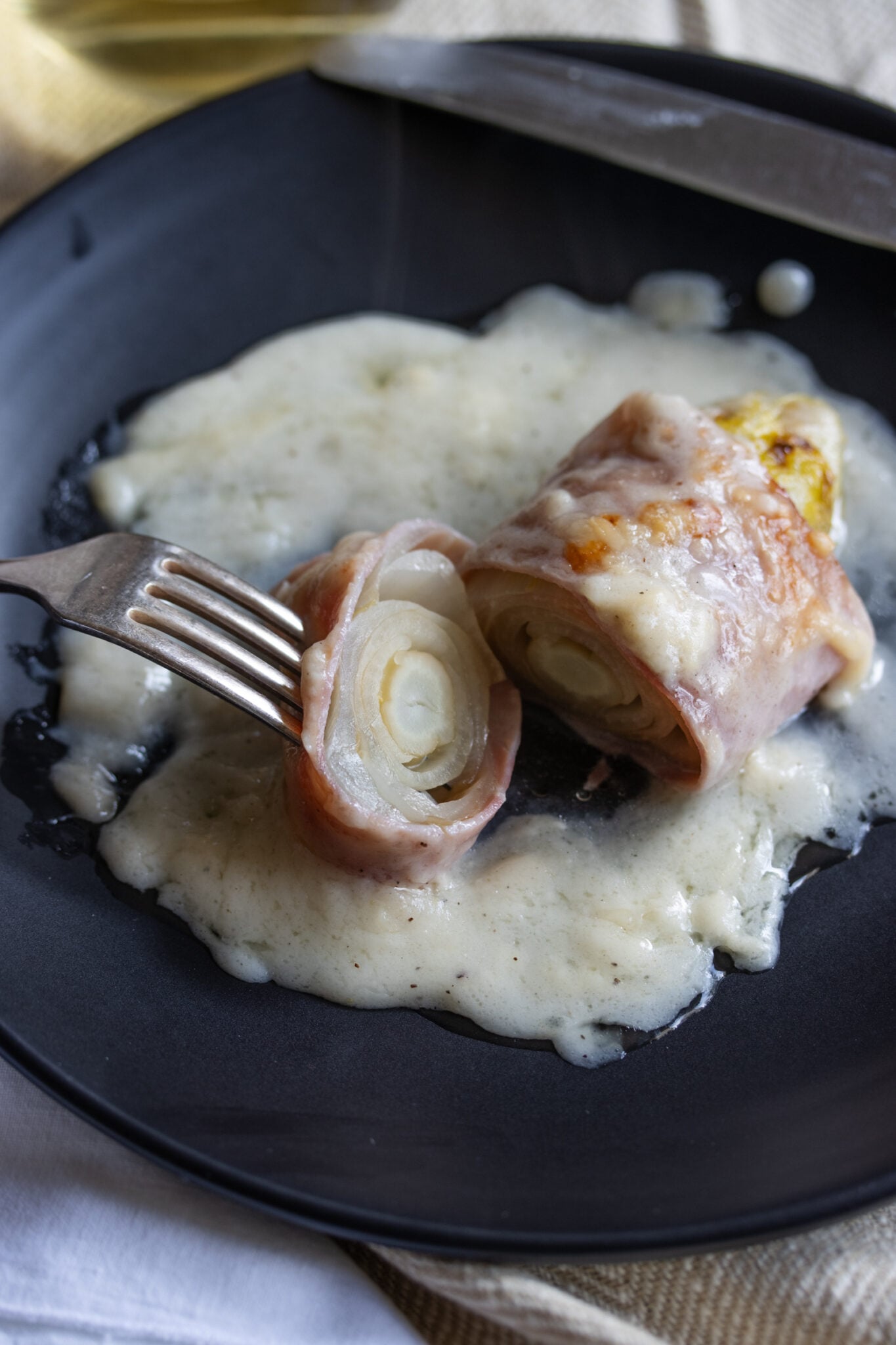 Endive Ham Gratin in a black plate with fork and cut