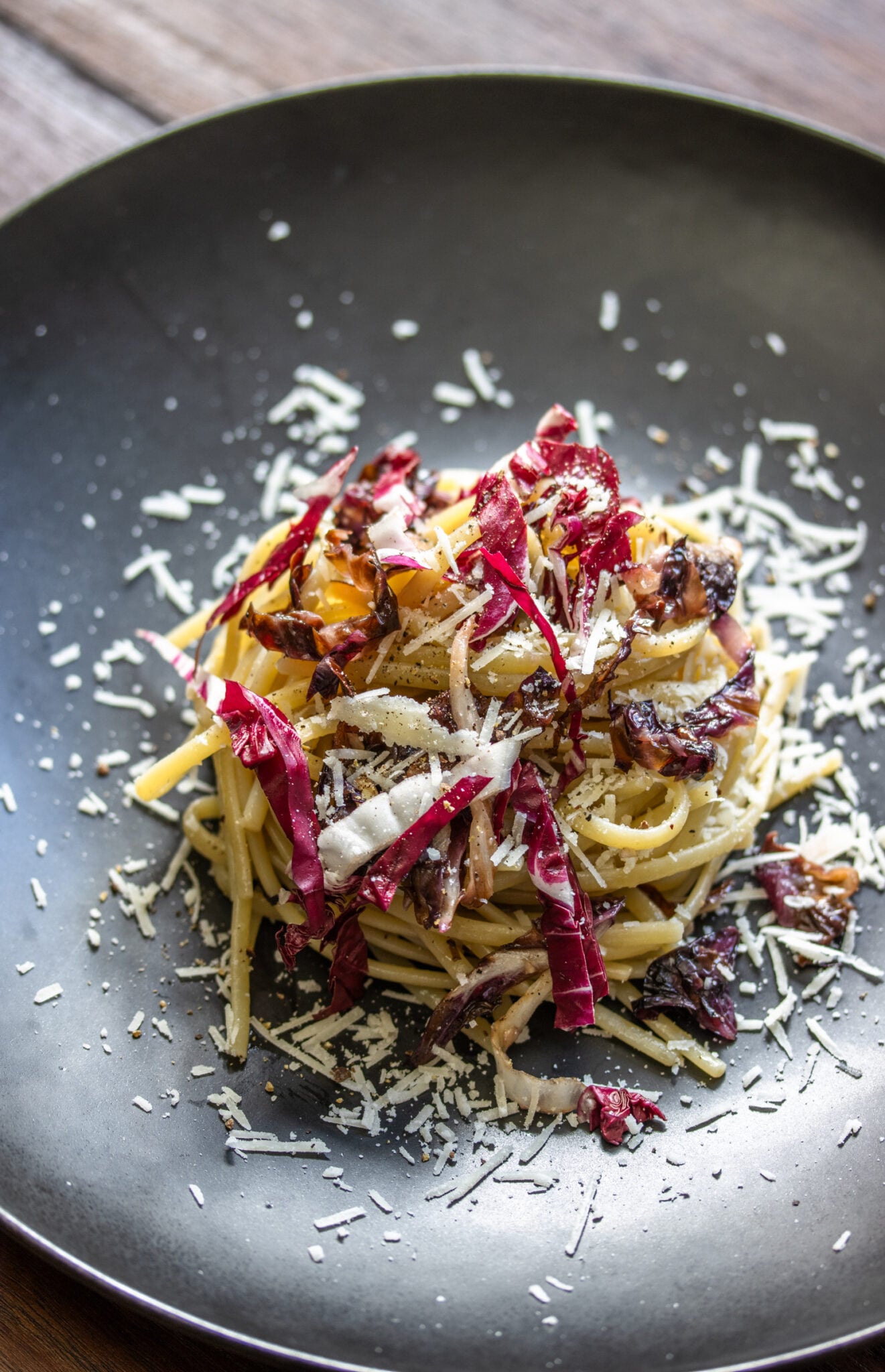 Linguine pasta, radicchio nad pecorino romano served on a black plate.