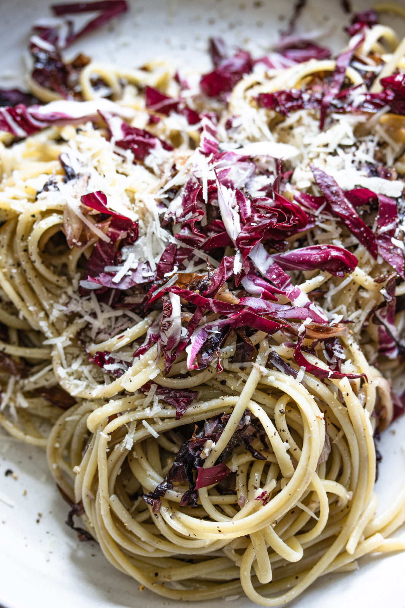 Radicchio pasta all ready and served with more grated cheese on a white plate.
