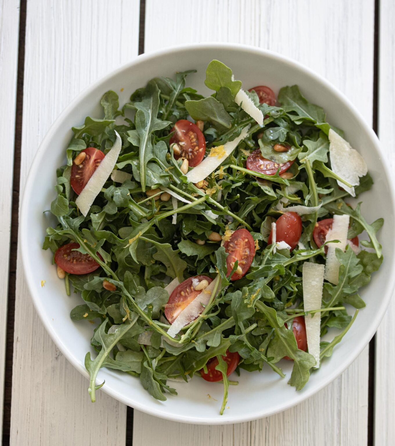 Tomato, arugula salad with shaved parmesan cheese served in a white plate with white background.