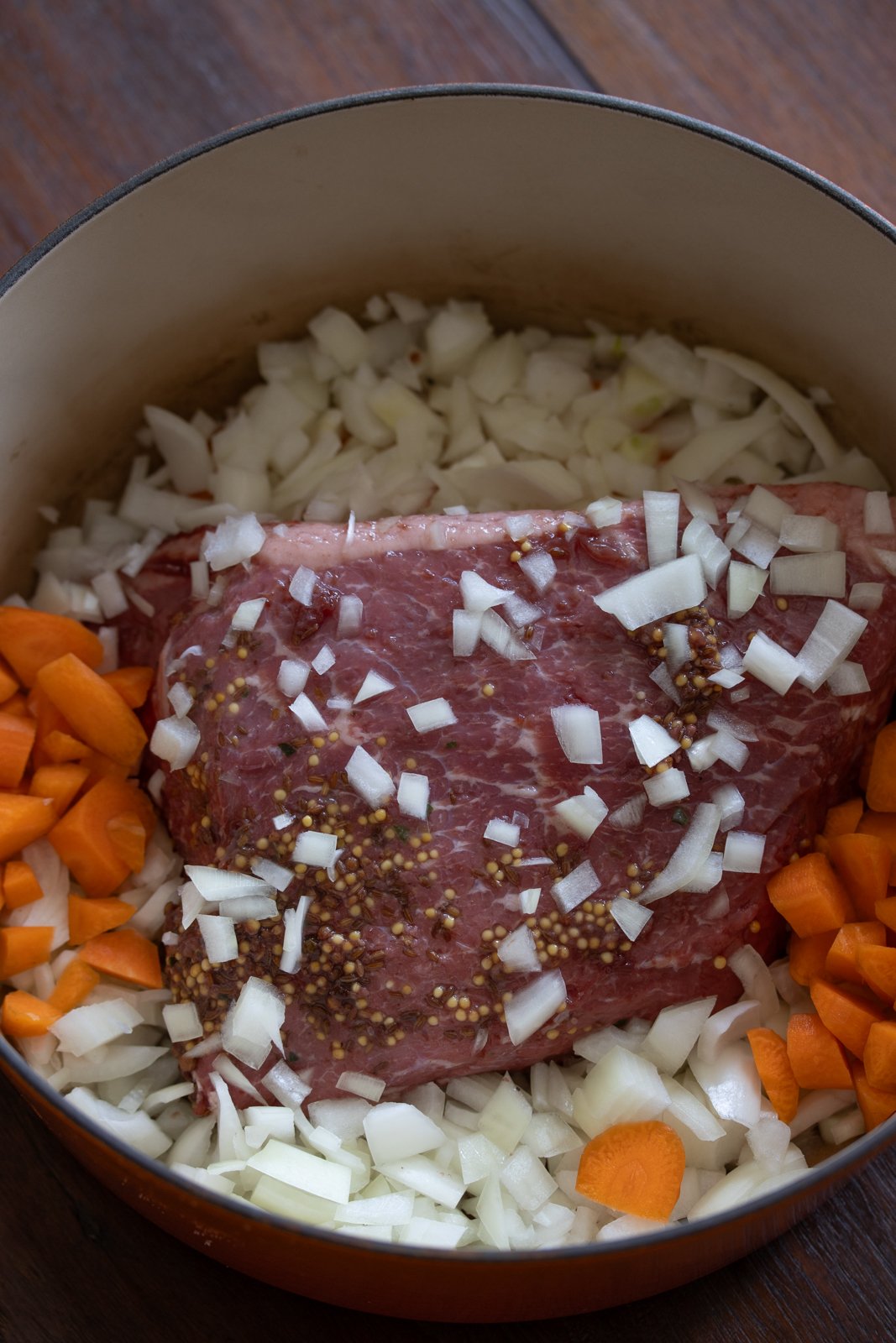 Corned Beef with Parsley Sauce in a dutch oven with carrots and chopped onions