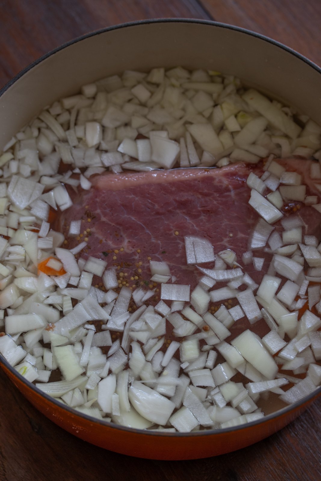 Corned Beef with Parsley Sauce in a dutch oven with carrots and chopped onions