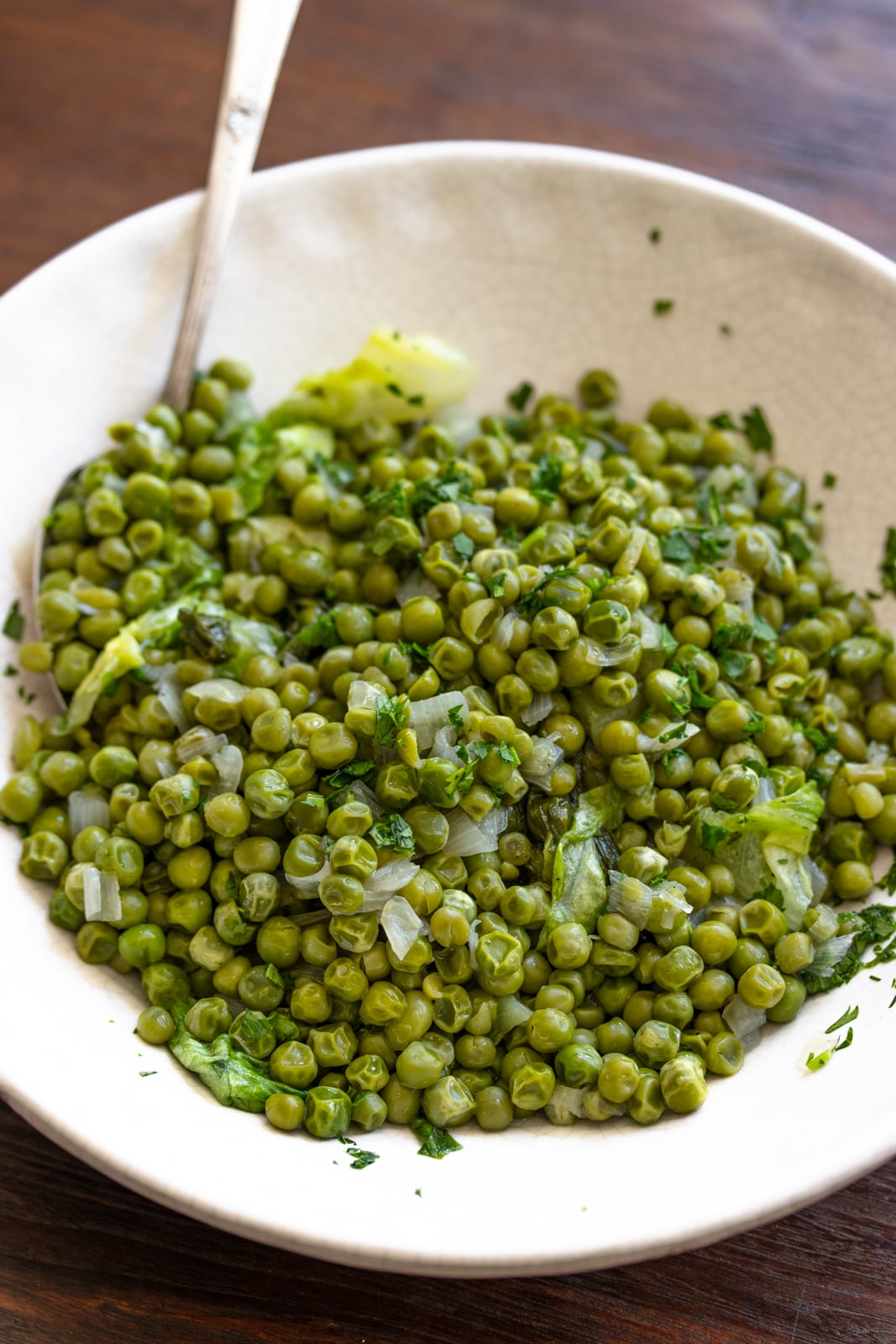 Petits Pois A La Francaise served in an off white serving dish with a spoon.