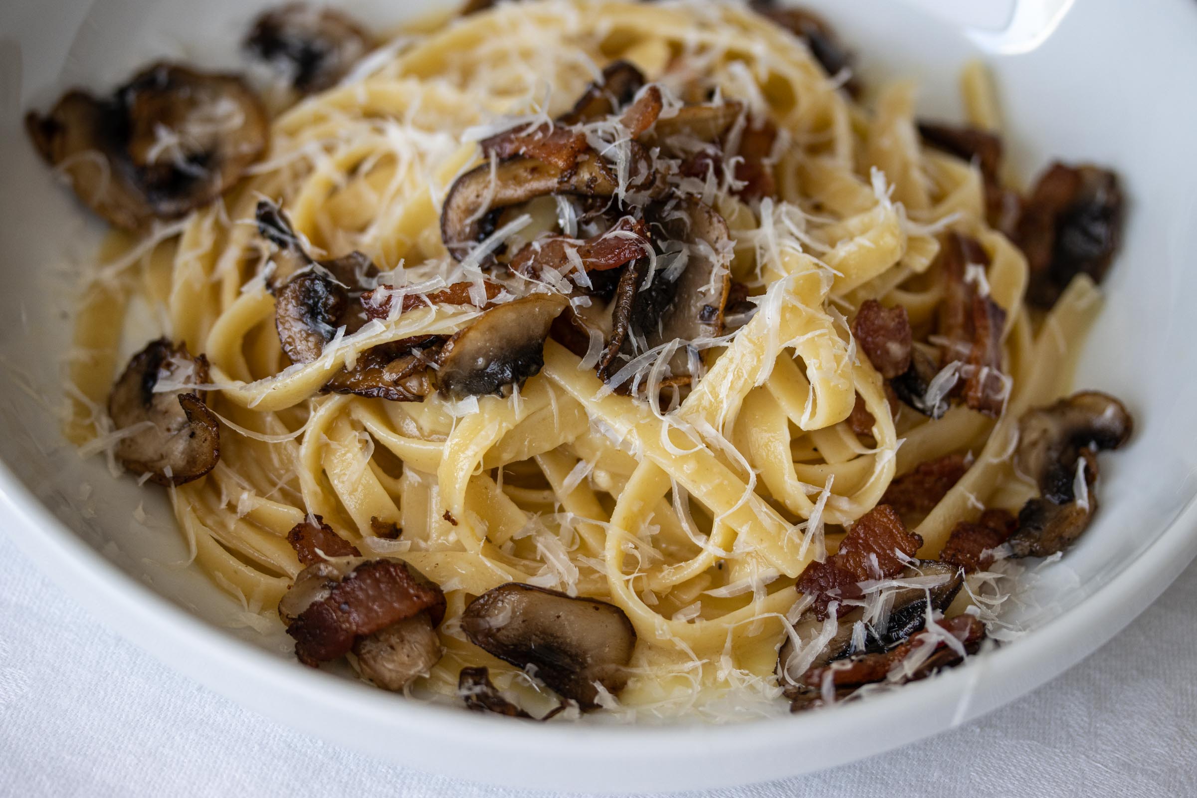 linguine, bacon and mushroom pasta in a serving white bowl