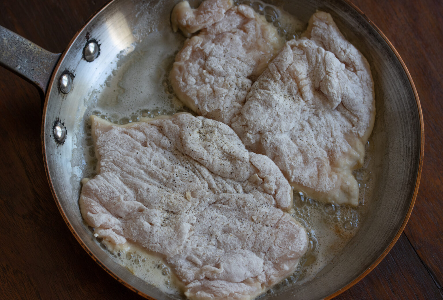 Floured chicken cutlets placed in a skillet