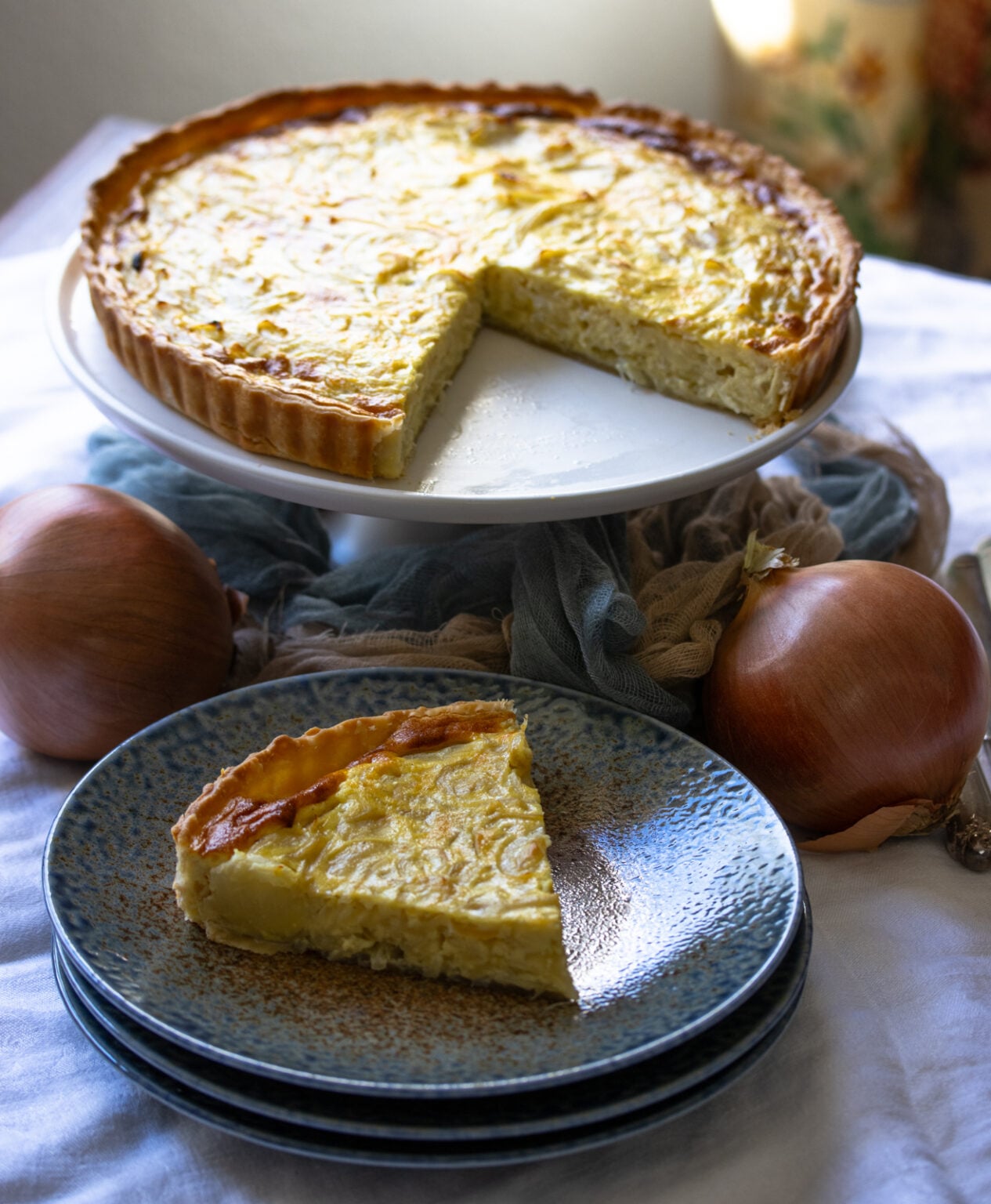 French Onion Tart - The Vintage Way French Onion Tart ready to be enjoyed and one slice served on a blue brown dish.