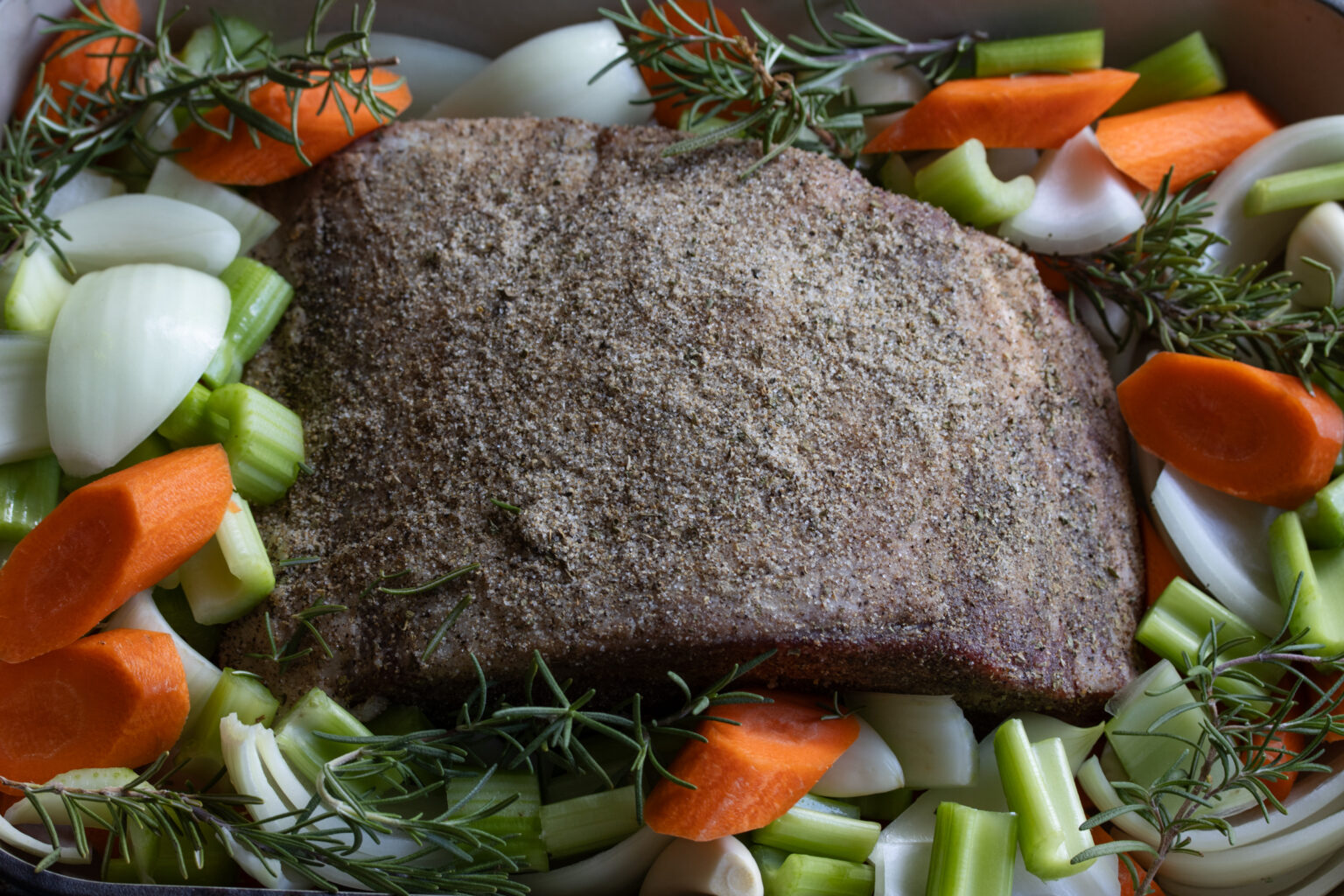 rib roast seasoned in a baking pan with vegetables around it