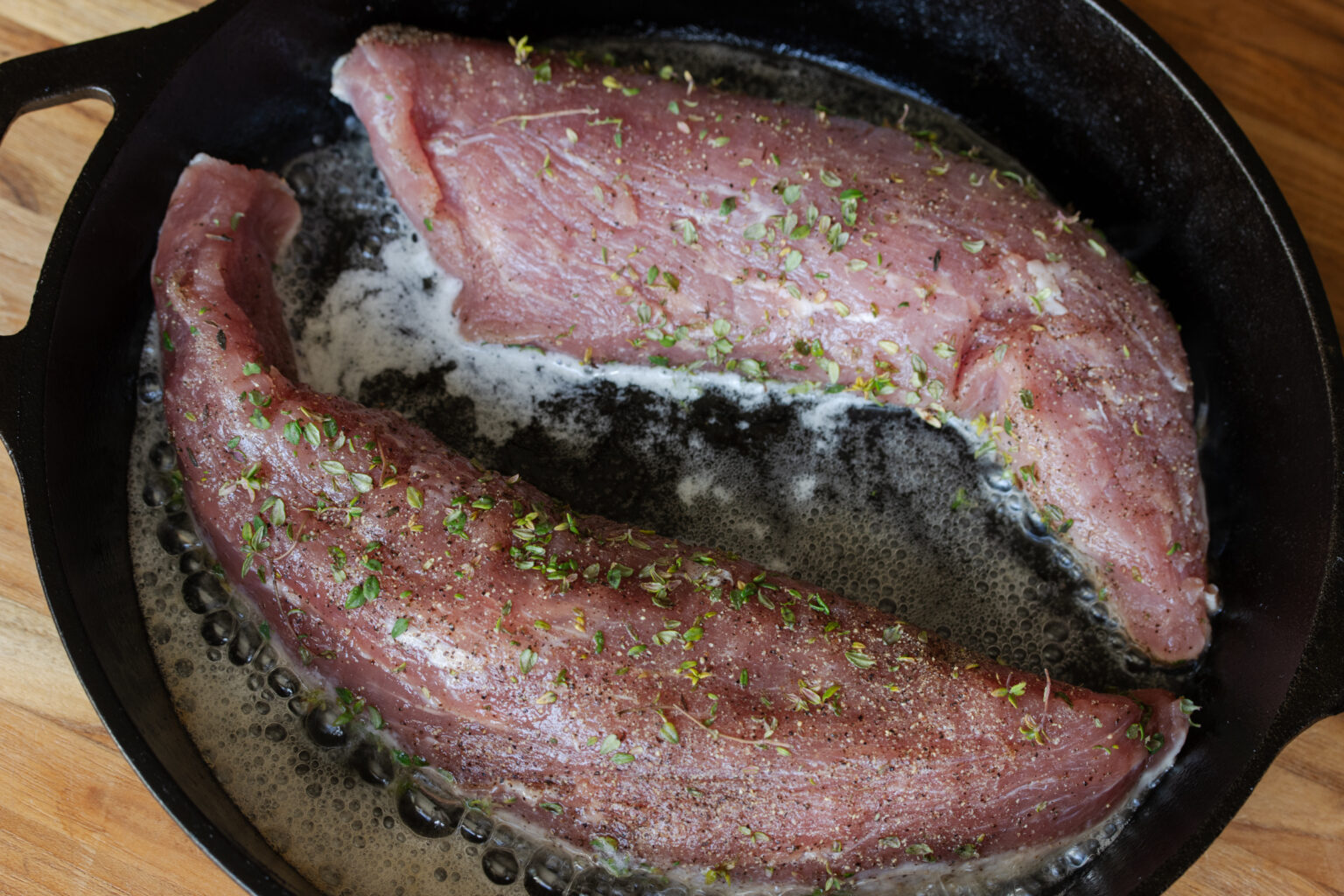 Pork tenderloin being seared with olive oil and butter.