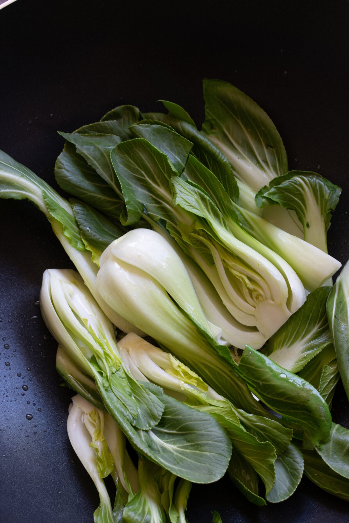 Bok choy pieces are added to the wok and seared until the green parts are wilting.