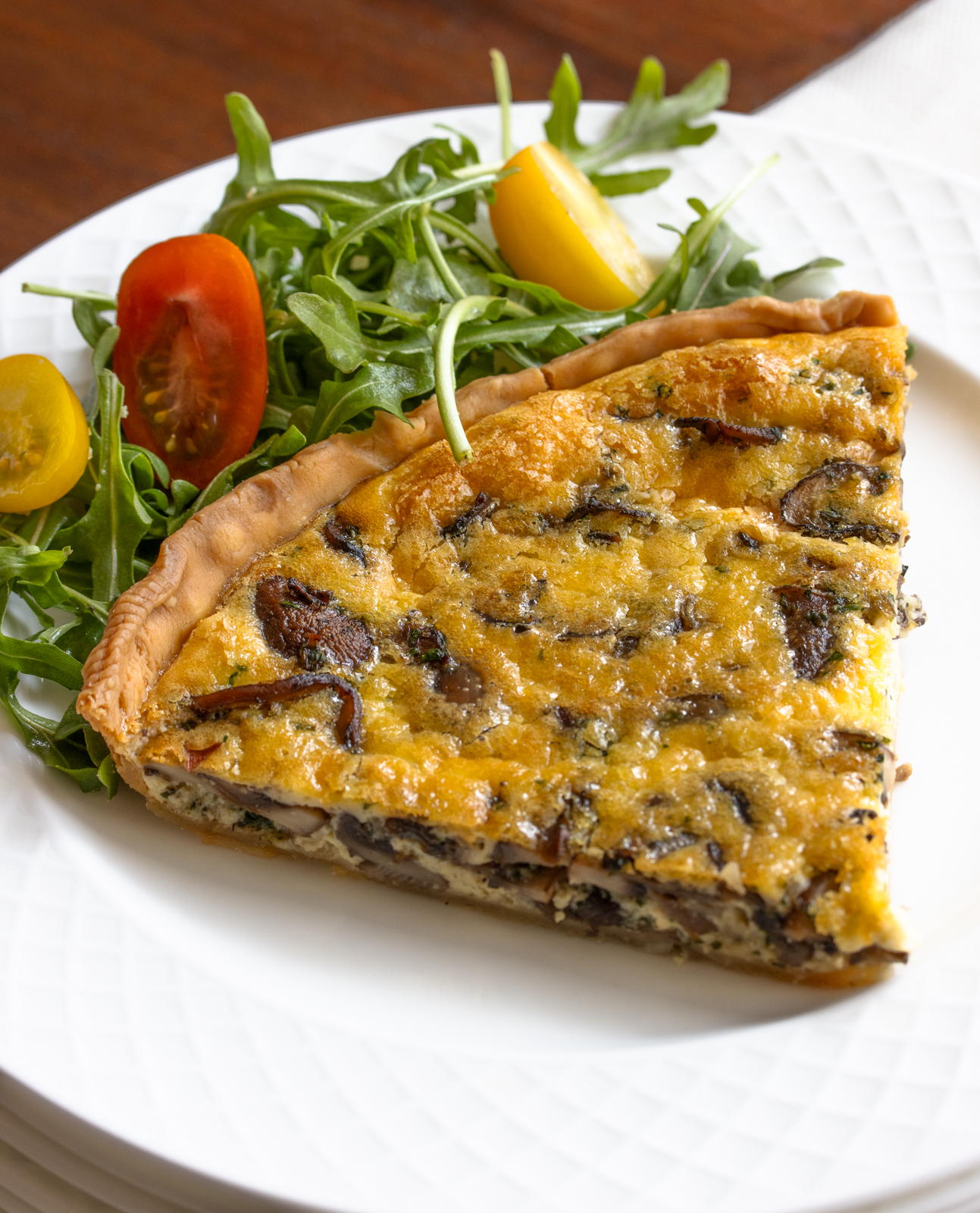 mushroom quiche slice on a white plate with green salad