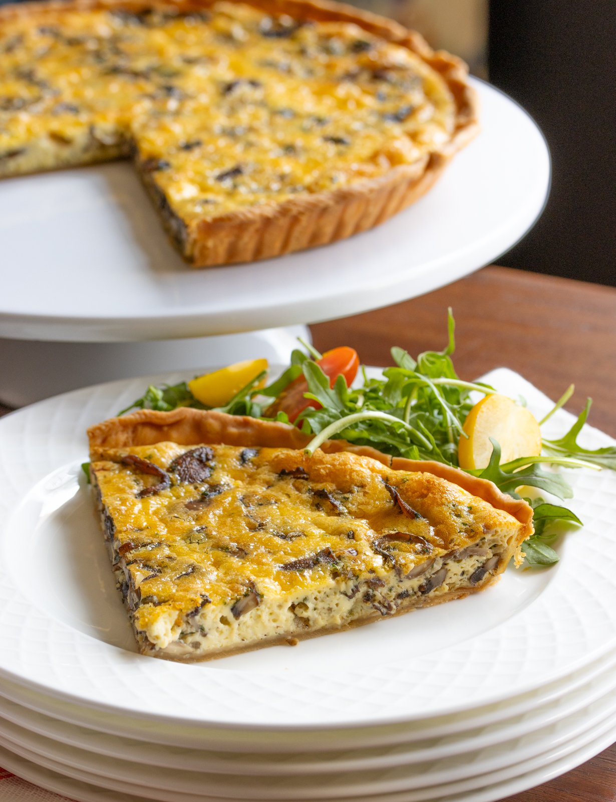 quiche on a cake stand and slice of quiche on a white plate