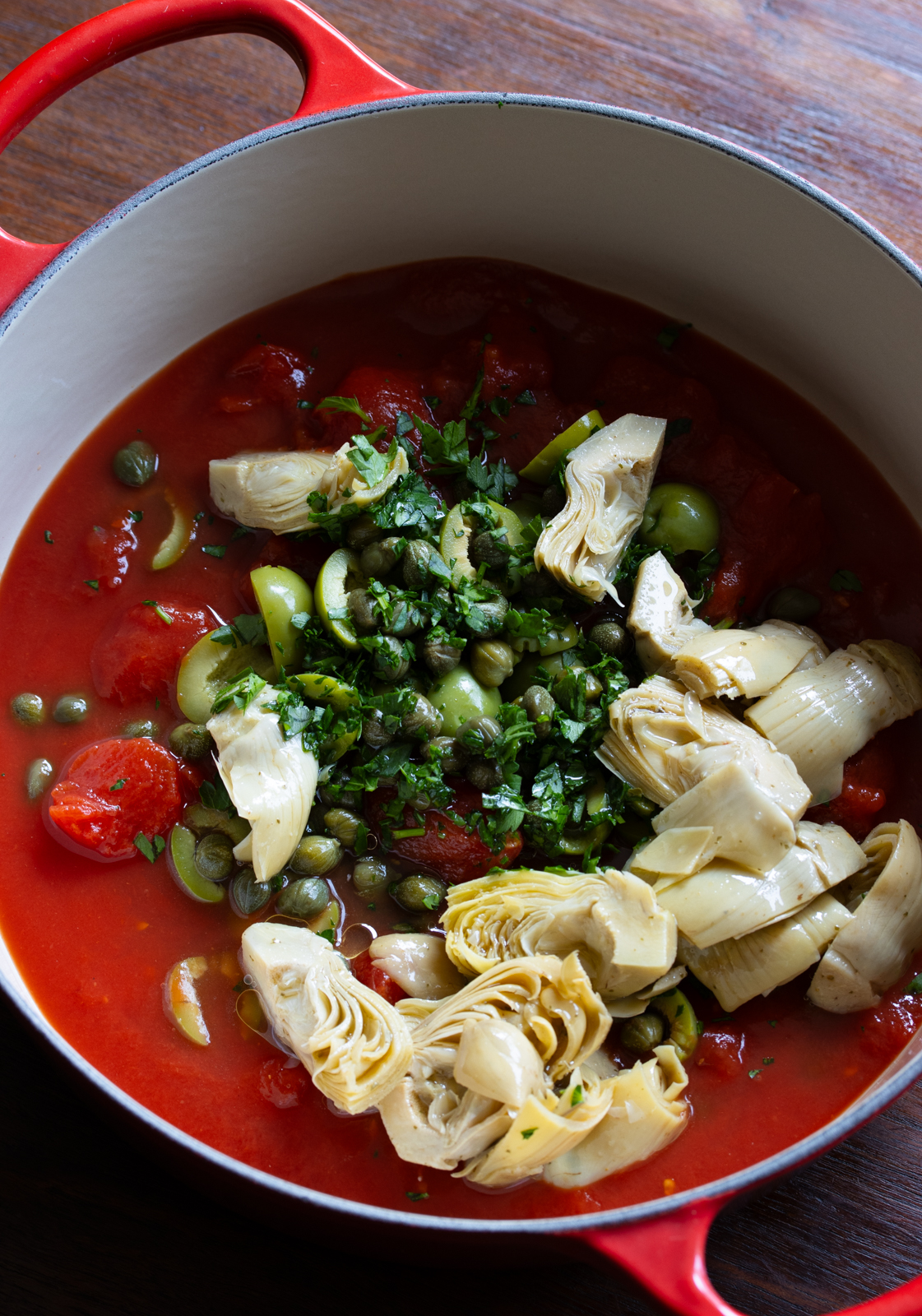 tomato, capers, olives, and artichokes in a pot to simmer