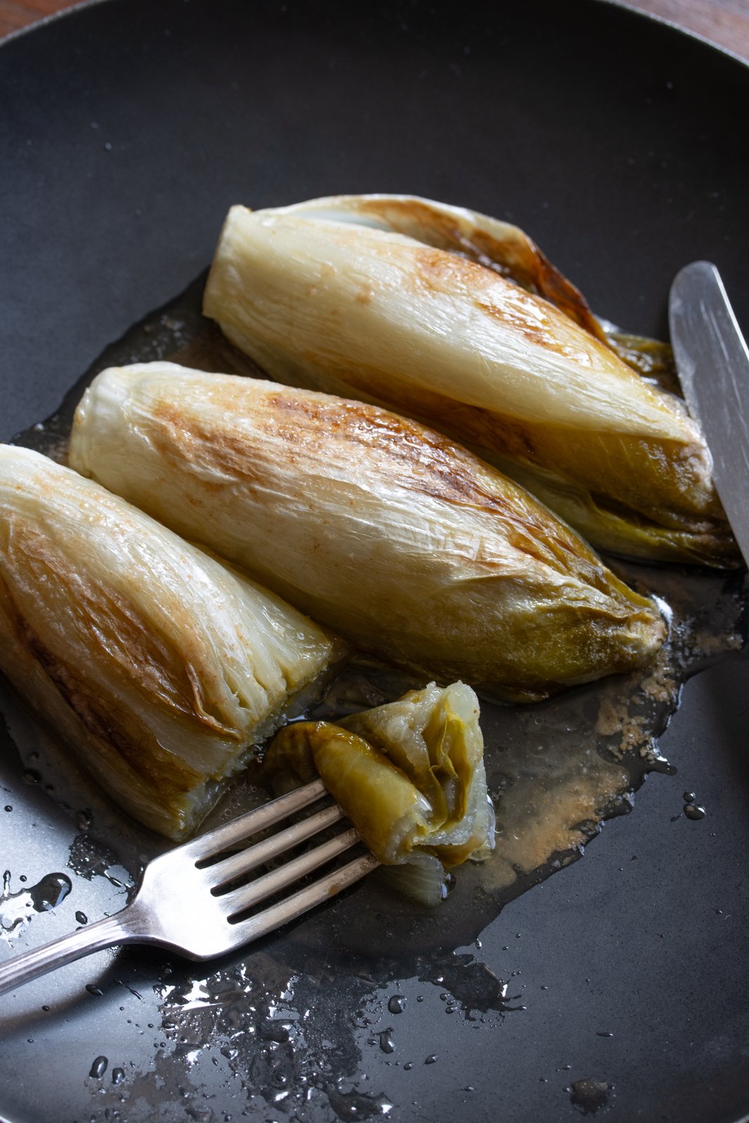 braised endives in a black plate with fork and knife
