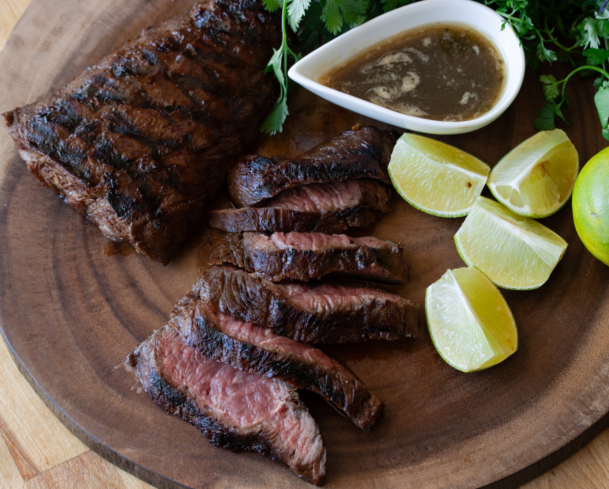 sliced flat iron steak on a wooden board with lime slices and marinade