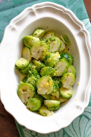 Brussels sprouts with lemon in a white serving dish sitting on a green napkin