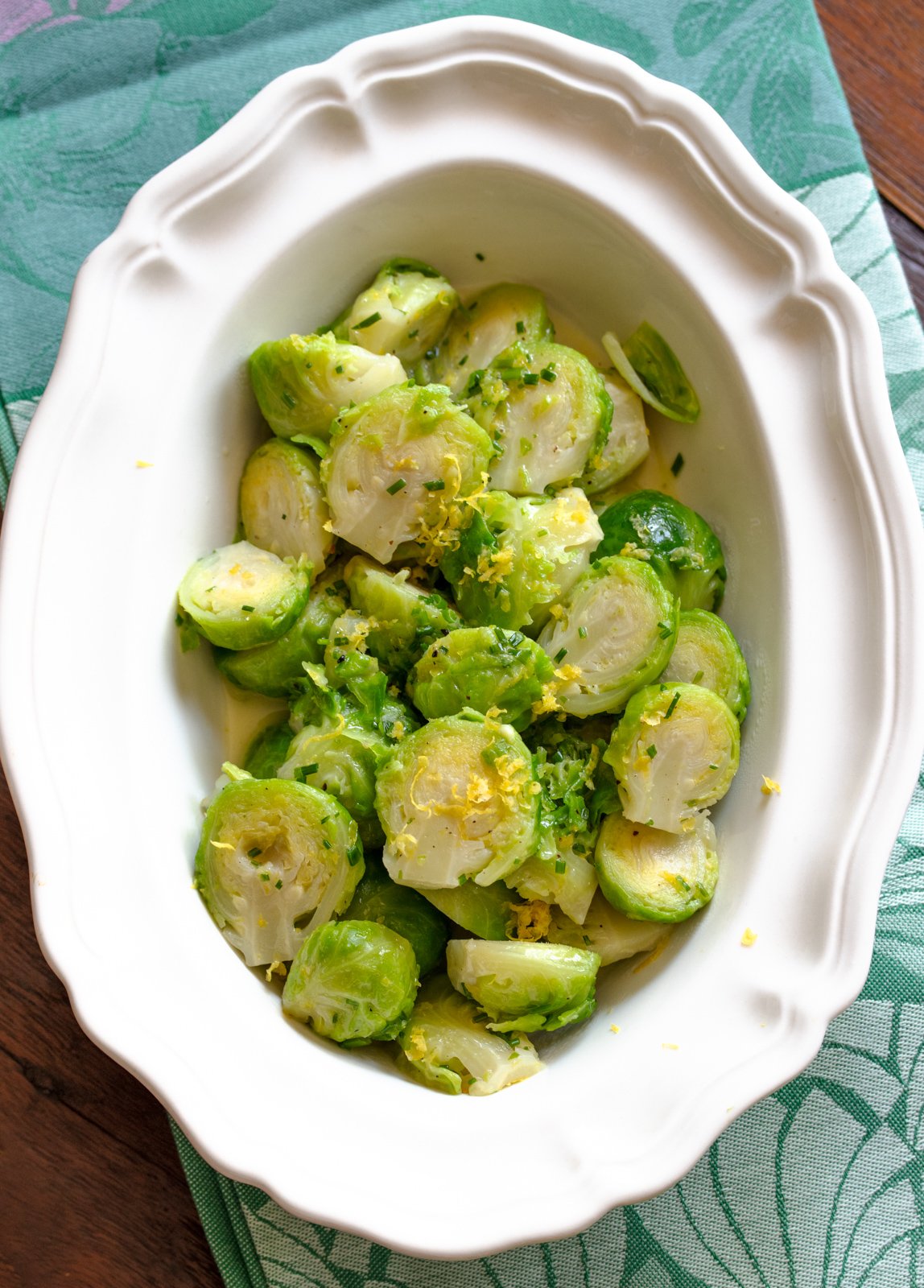 Brussels sprouts with lemon in a white serving dish sitting on a green napkin
