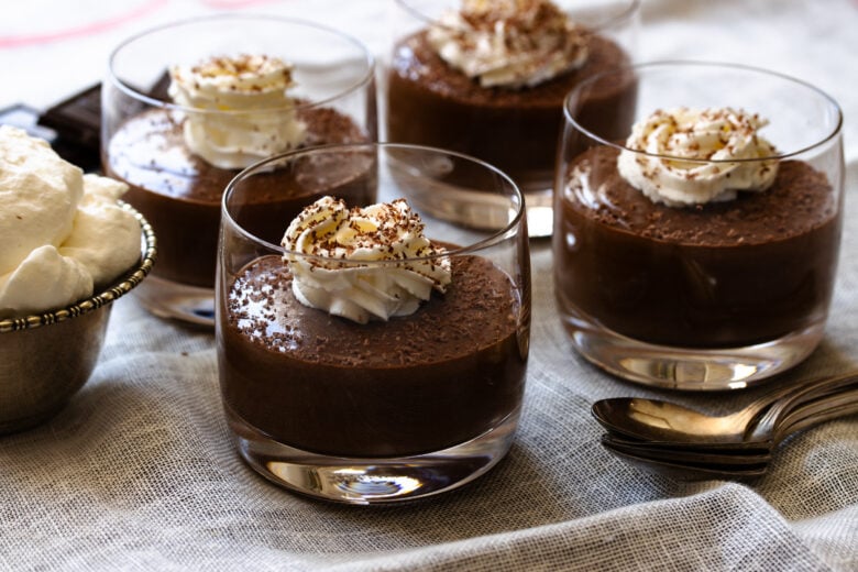 Four chocolate mousse served in small glasses topped with whipped cream.