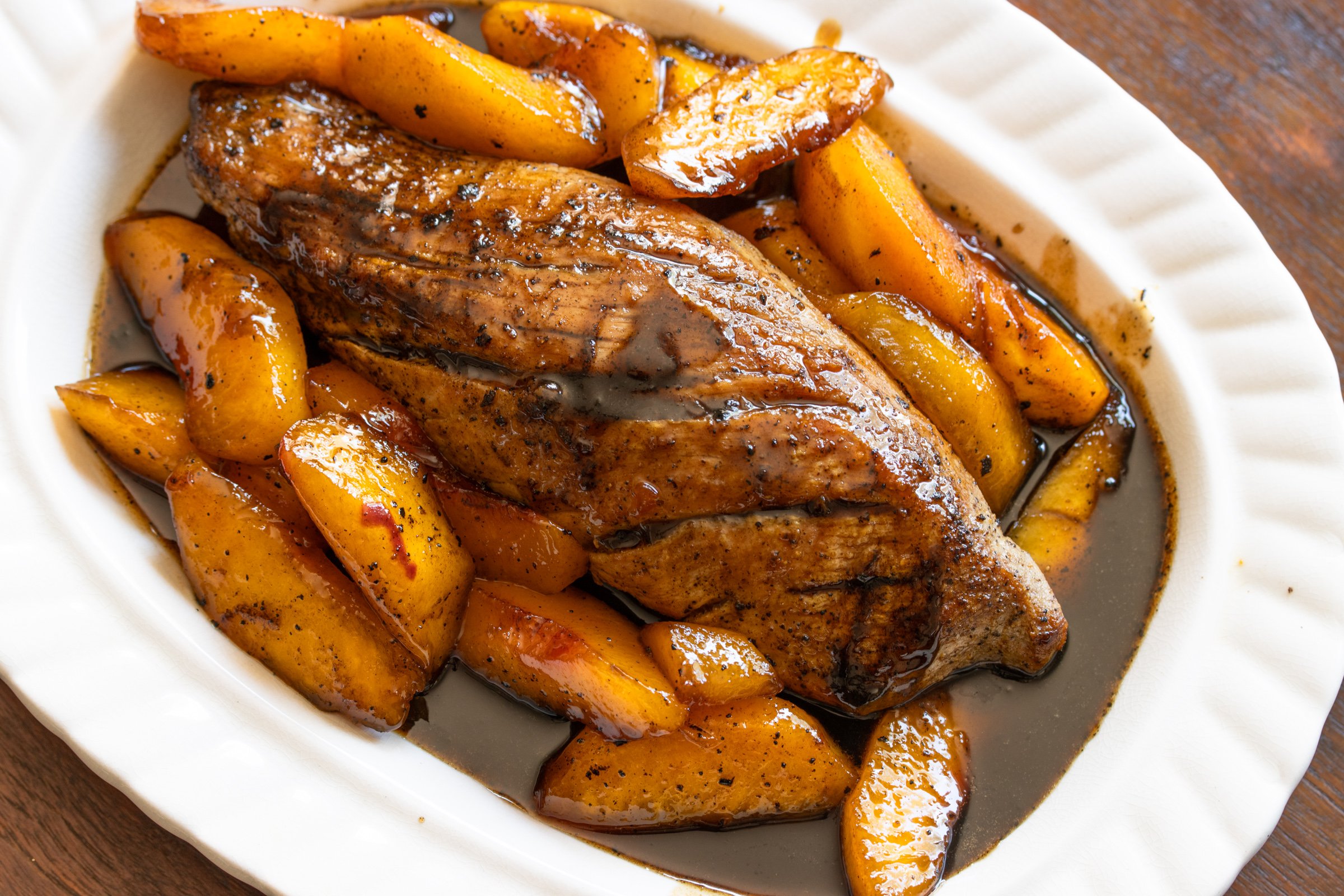 Pork tenderloin with peach glaze surround it in a white scalloped serving dish.