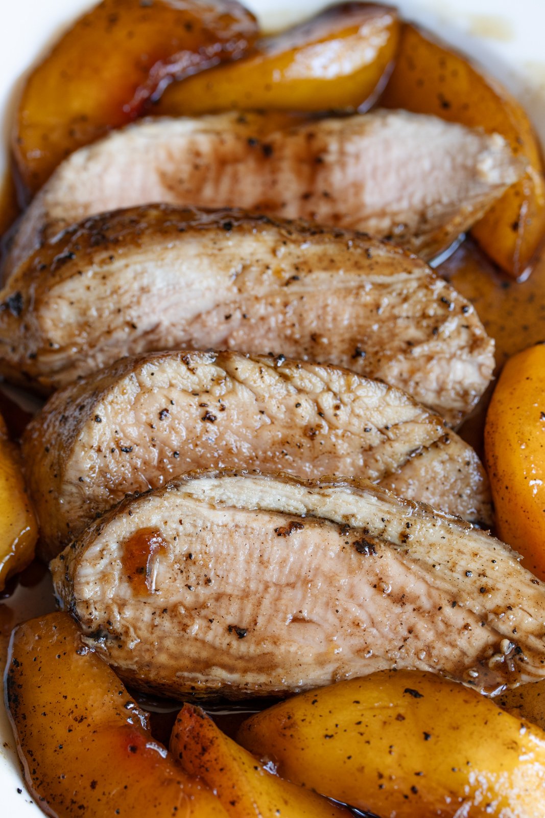 Sliced glazed pork tenderloin surrounded by peaches served on a white dish