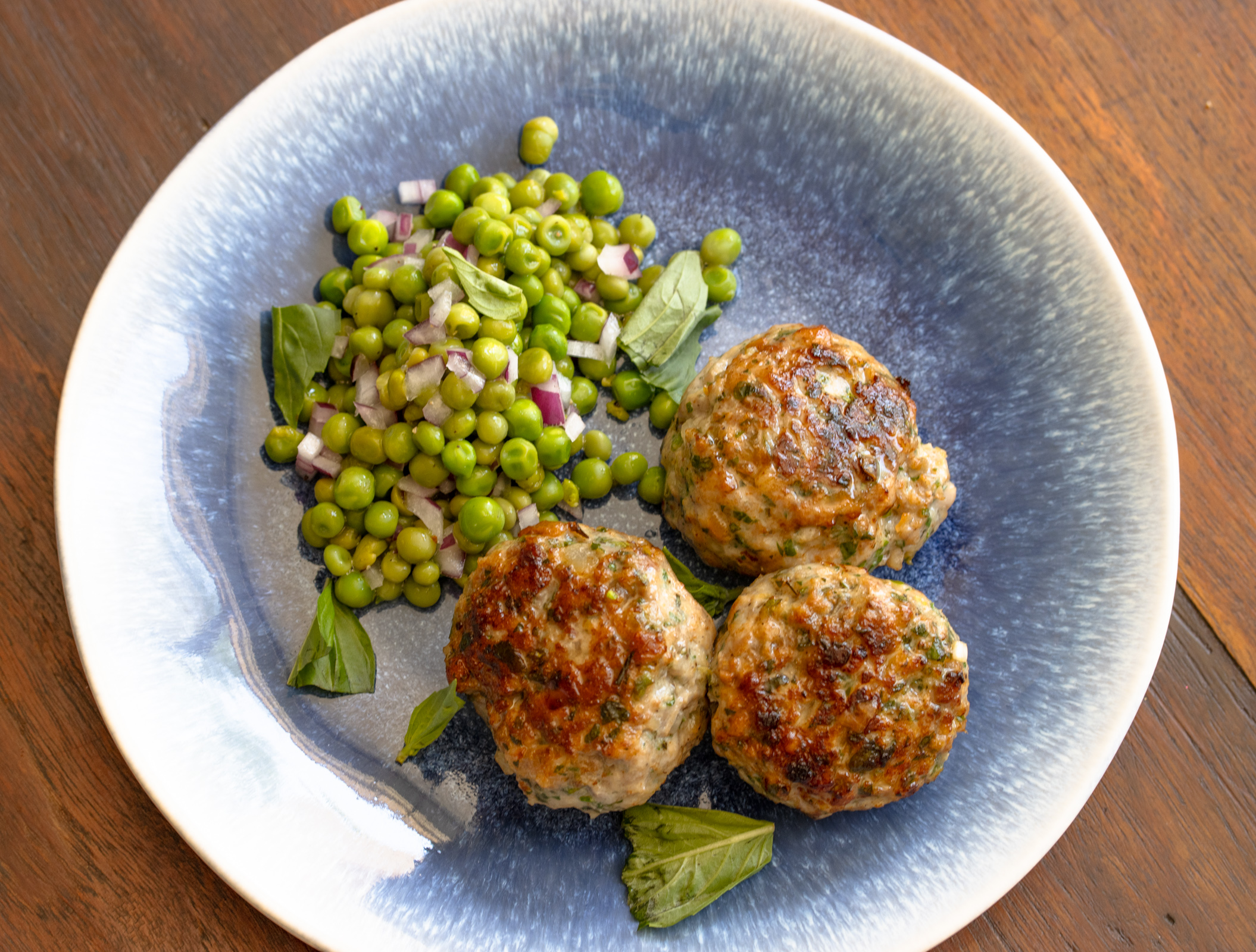 Three chicken meatballs on a light blue dish with peas alongside.