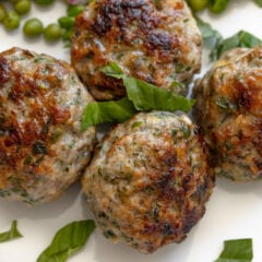 Close up of cooked ground chicken meatballs presented on a white plate.