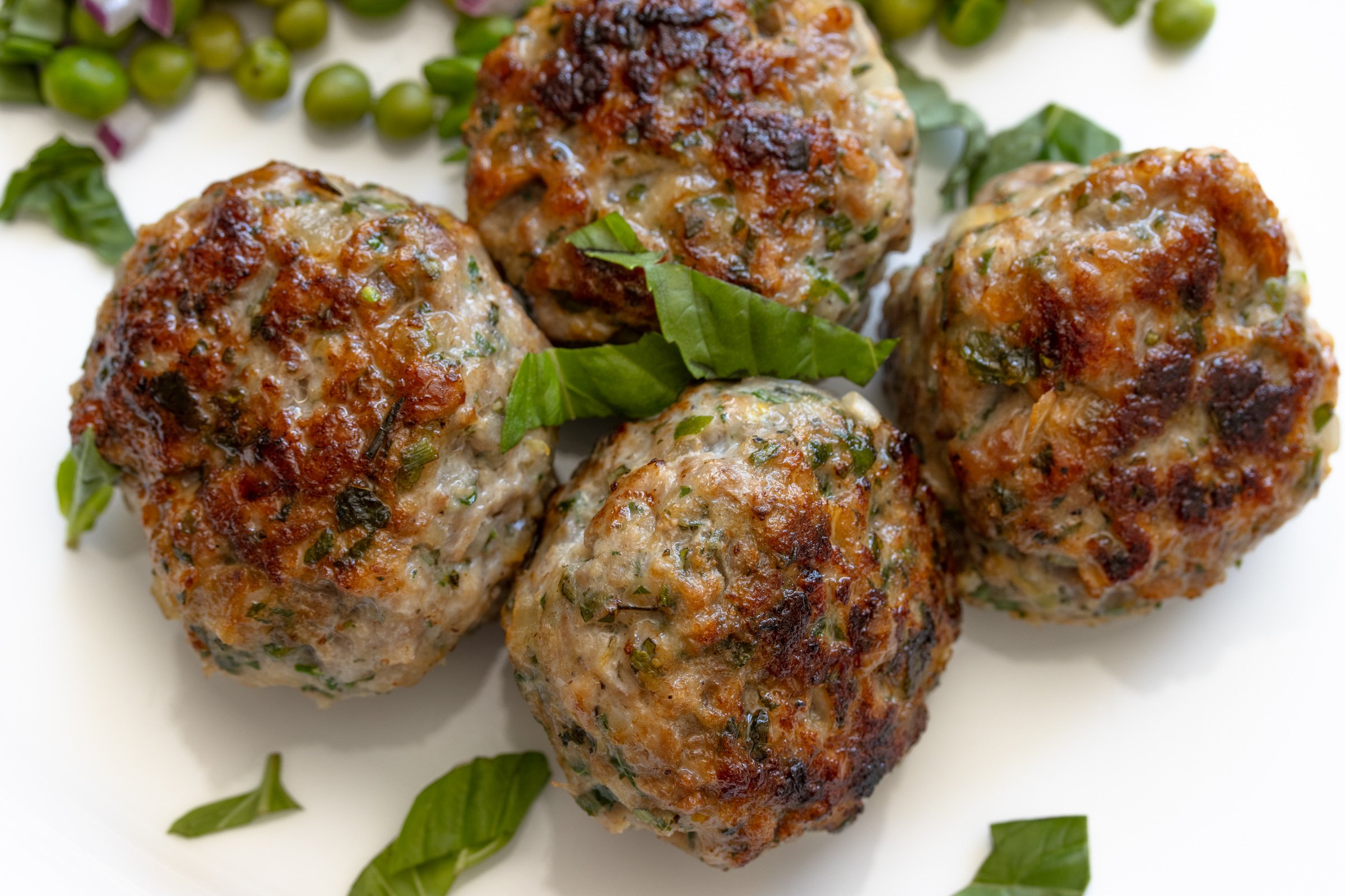 Close up of cooked ground chicken meatballs presented on a white plate.