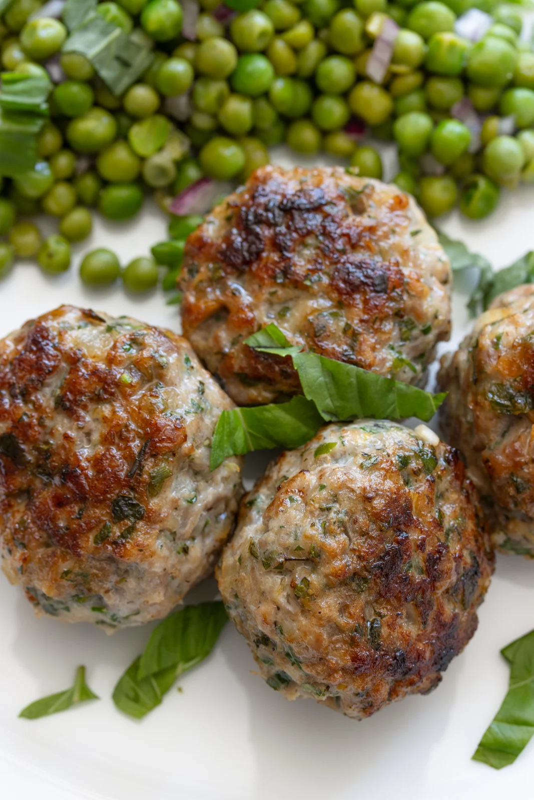 Four chicken meatballs placed on a white plate with peas in the background.