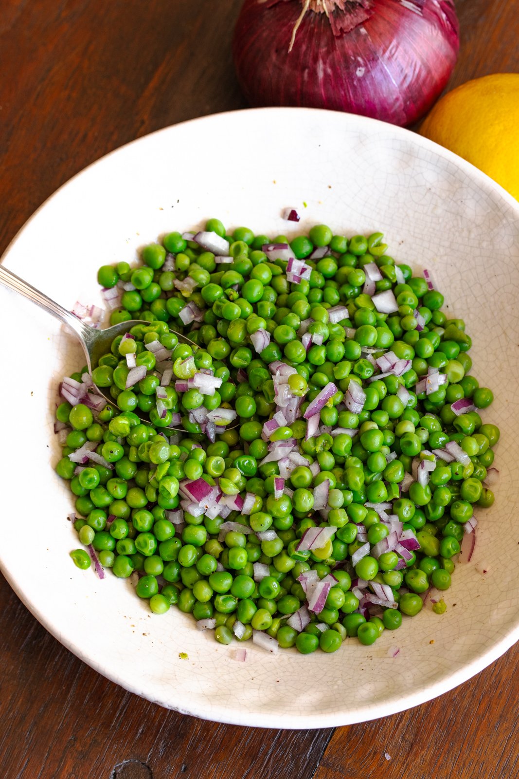 Cold pea salad served in a plate with a serving spoon and ready to be enjoyed.