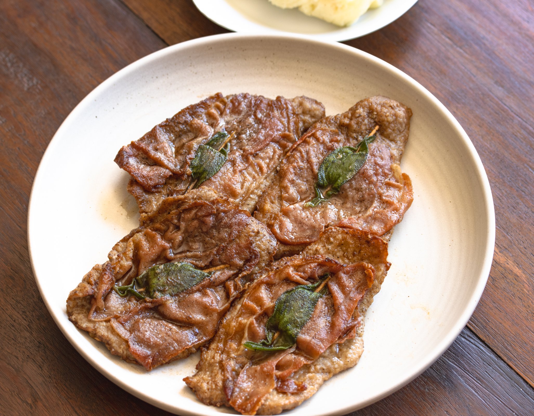Cooked veal saltimbocca in a white serving plate.