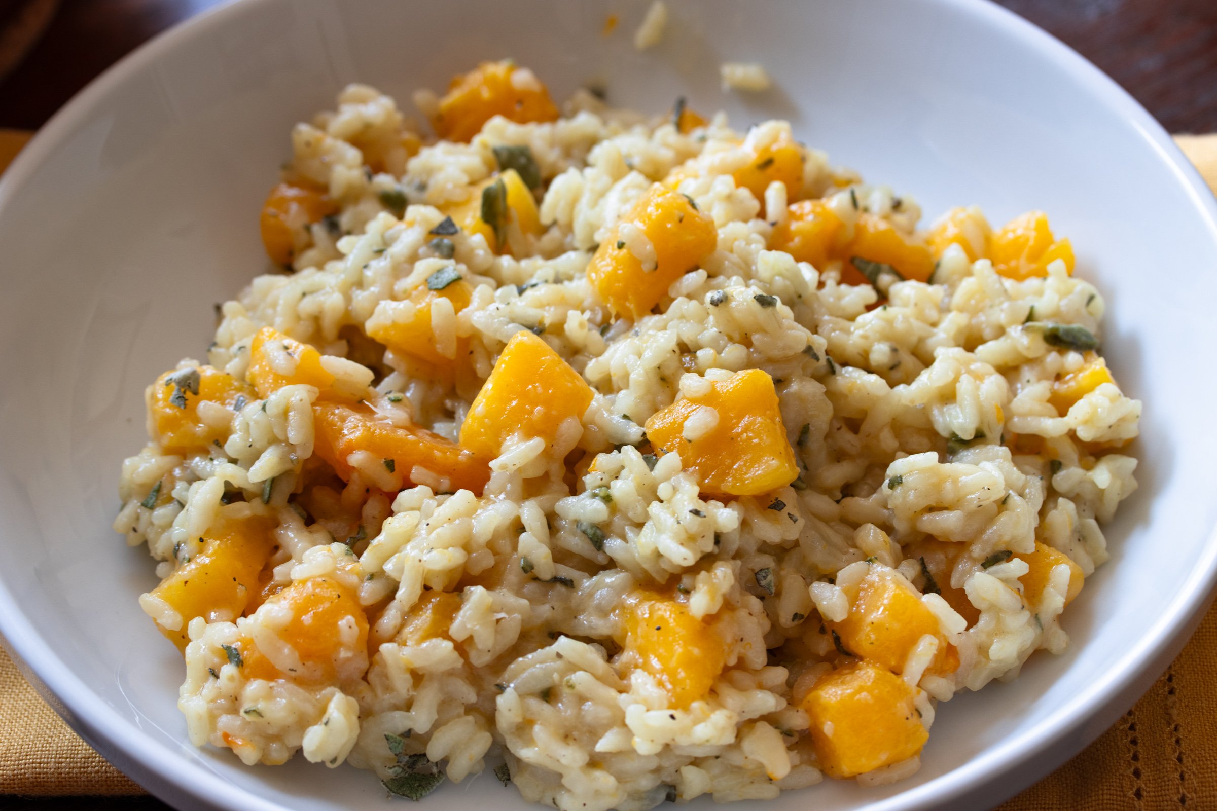 Warm butternut risotto served in a white plate with grated parmesan cheese over it.