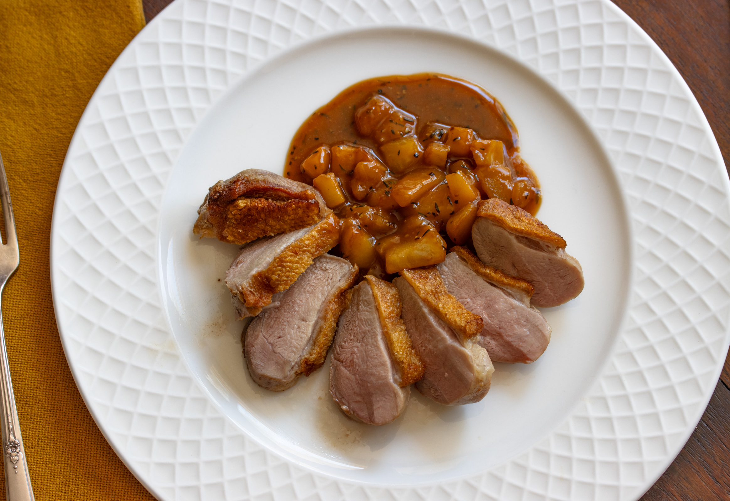 Duck breast sliced and arranged on a white plate with the pears and sauce poured around it. 