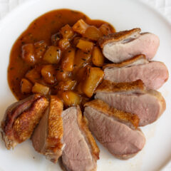 Crispy duck breasts sliced on a white plate.