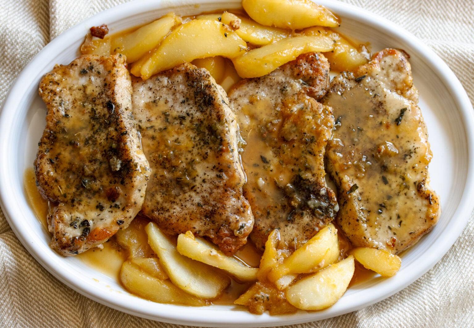 Pan friend bonelsess pork chops served alongside peasr in a white plate. 