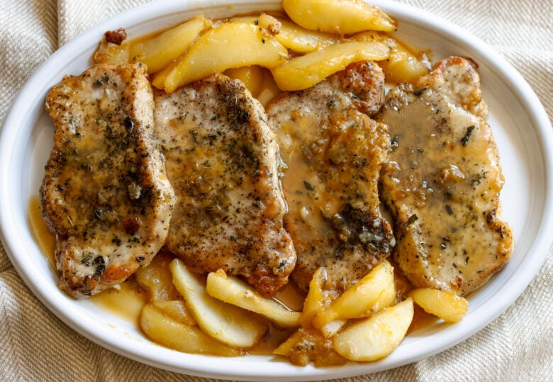 Pan friend bonelsess pork chops served alongside peasr in a white plate.
