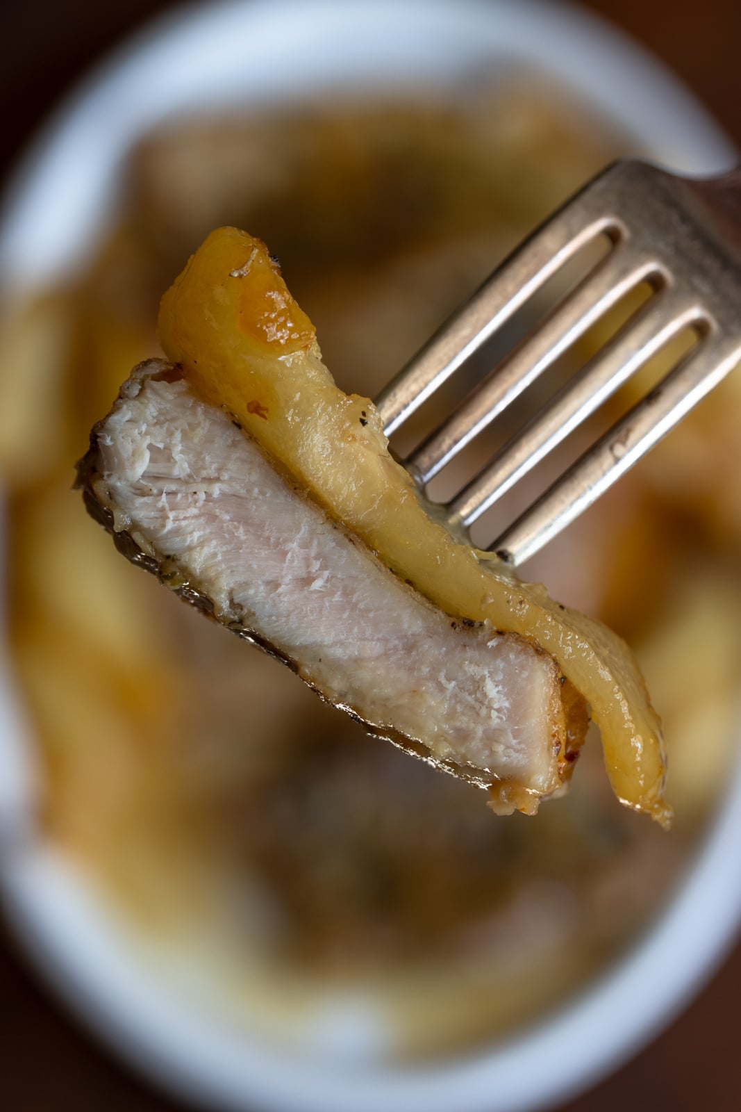 A fork containing a piece of pork with a caramelized pear. 