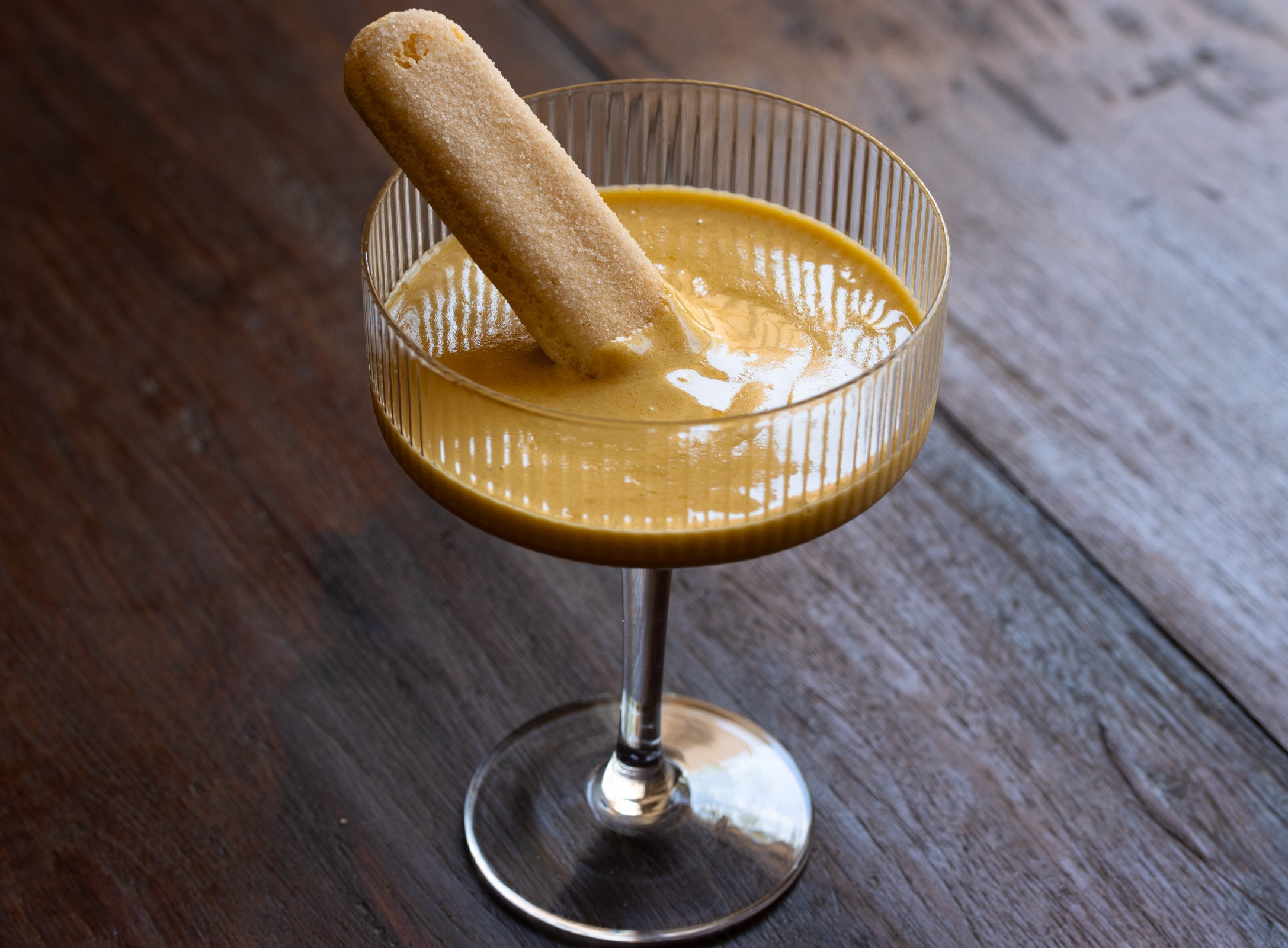 Zabaione with a savoiardi cookie on a wooden table.