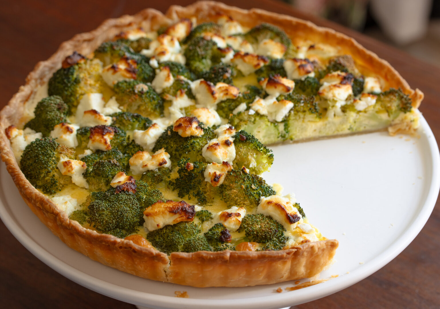 Baked broccoli quiche on a serving platter with a slice removed.