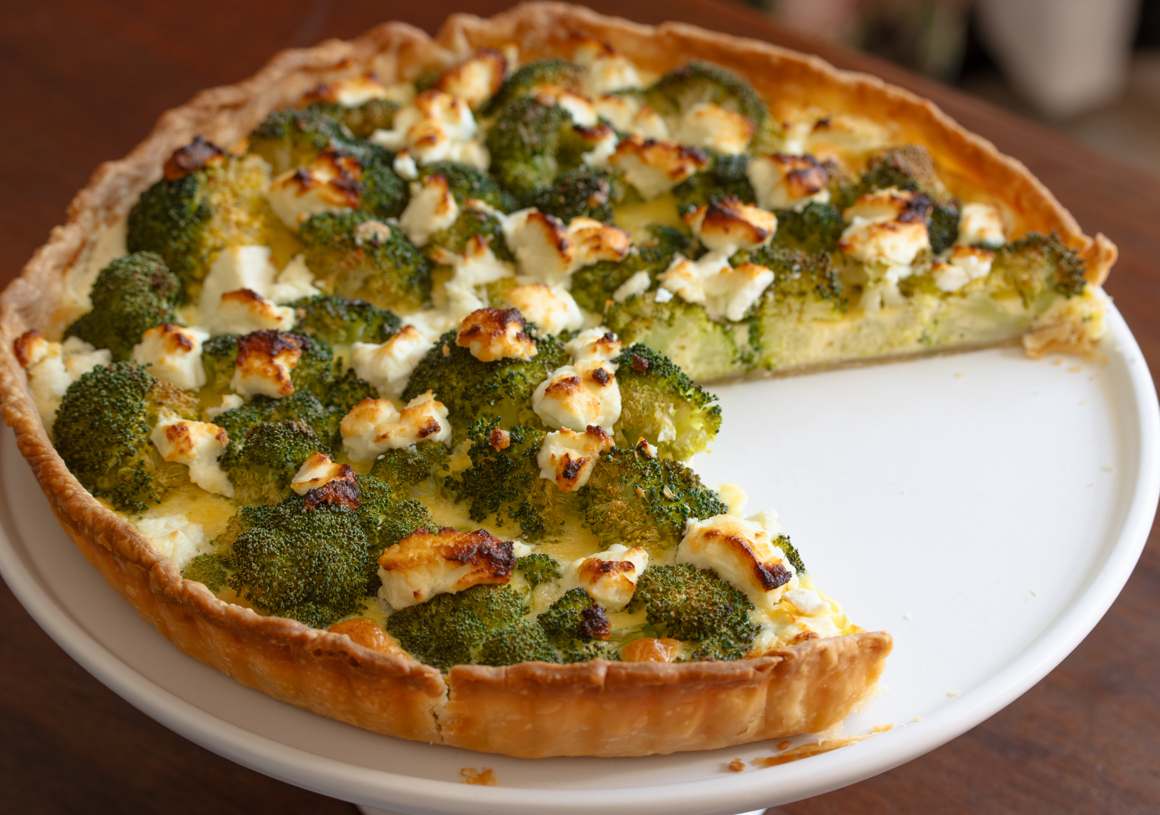 Baked broccoli quiche on a serving platter with a slice removed.