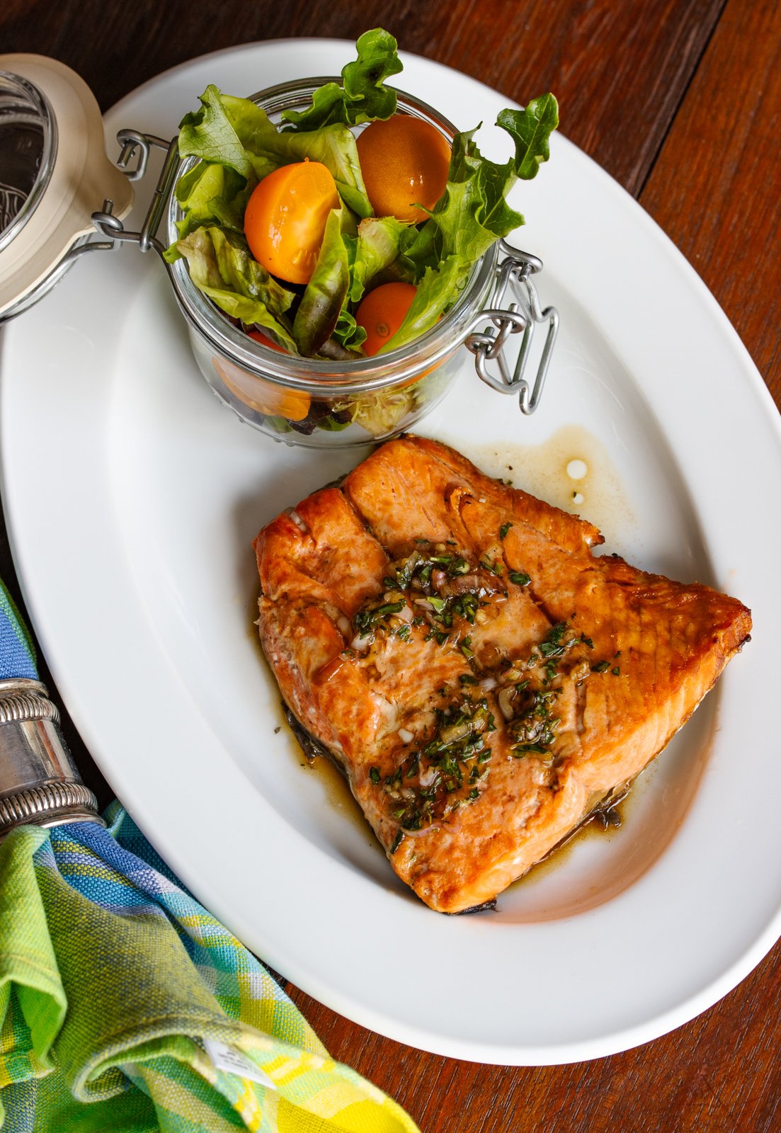 Broiled salmon recipe with tarragon sauce served on an oval white plate and salad in a small container.