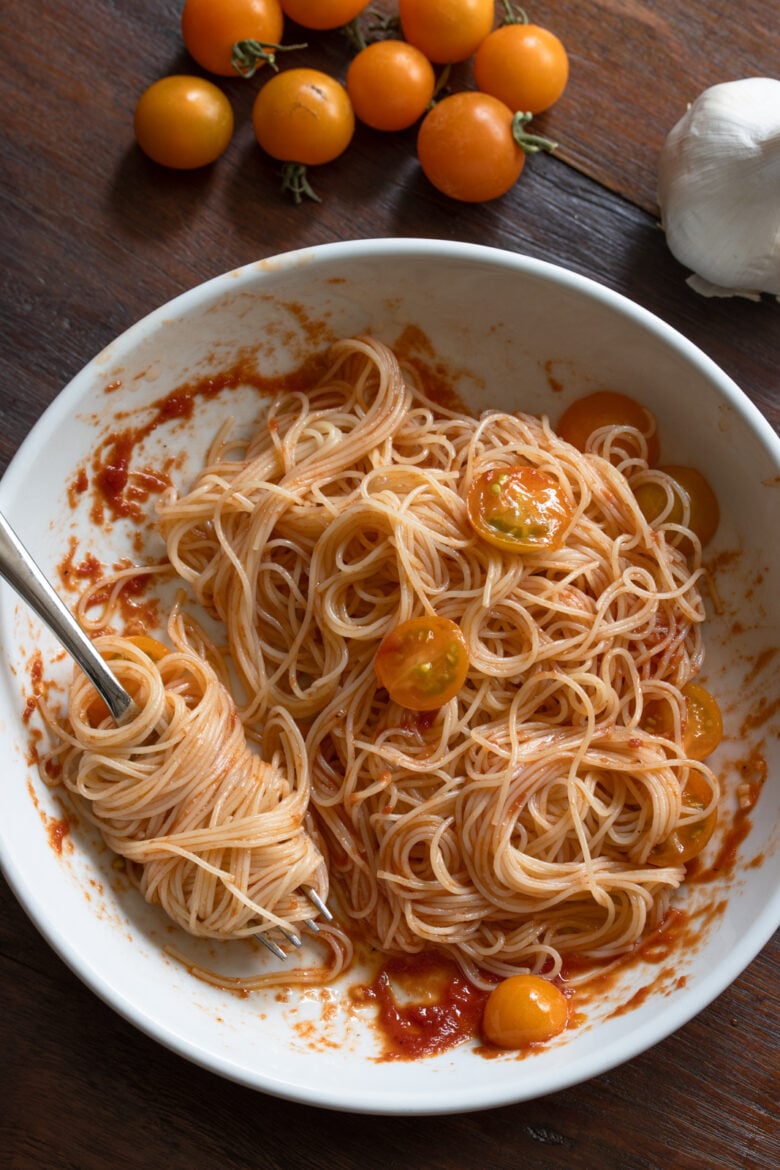 Angel hair pasta with the reduced tomato puree in a white serving plate.