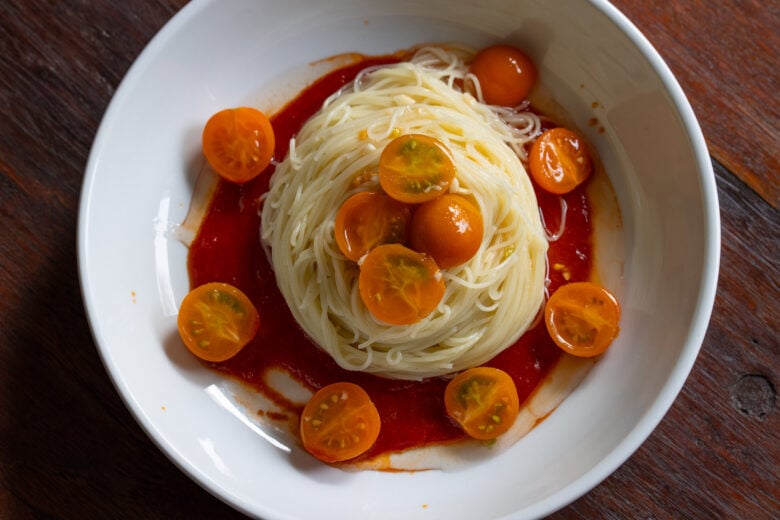 Angel hair pasta in a white dish, over tomato reductions and with cherry tomatoes added over the top.