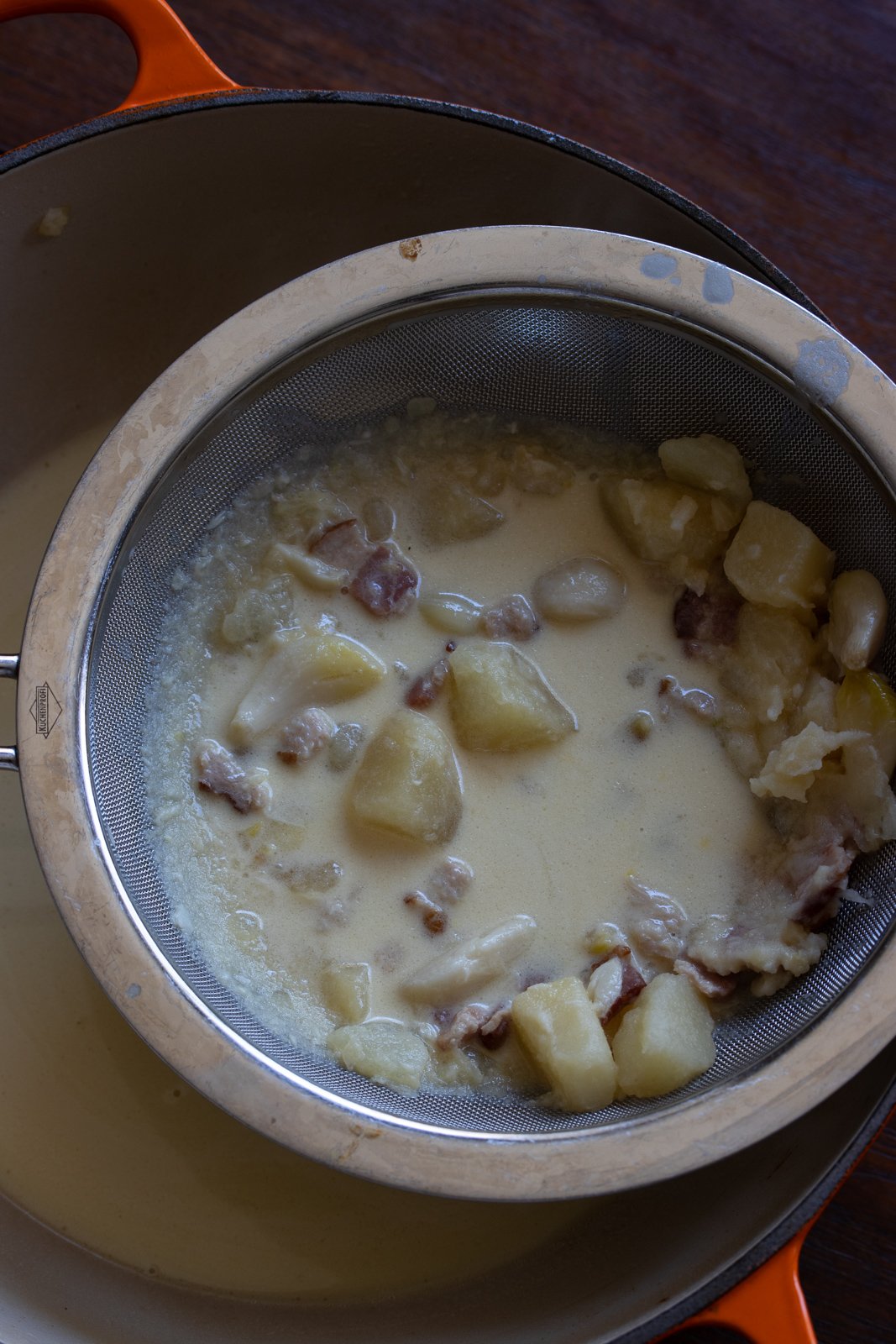 Potatoes, garlic and bacon being pressed against the fine mesh colander to retrieve the garlic pulp. 