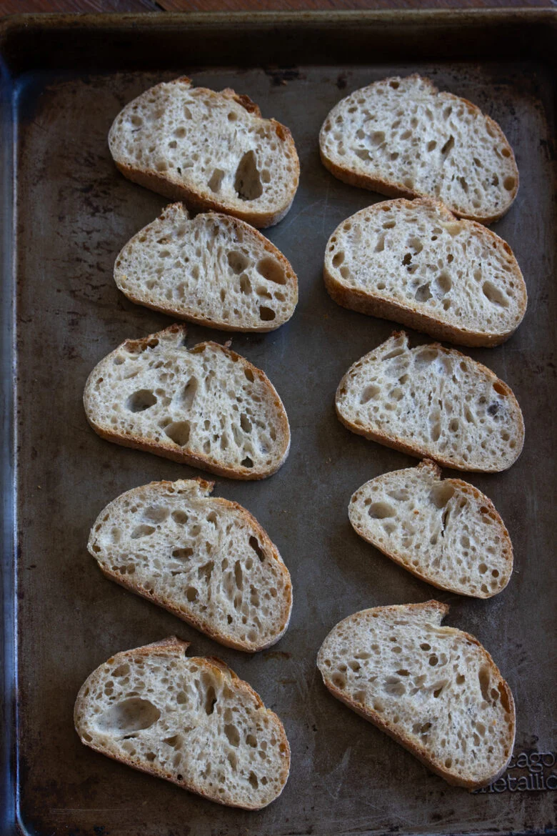 Baguette sliced and on a baking sheet ready to be toasted in the oven.